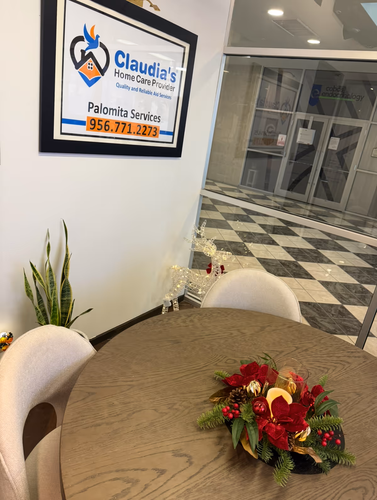 Lobby area with round wooden table, holiday centerpiece, potted plants, and Claudia's sign.