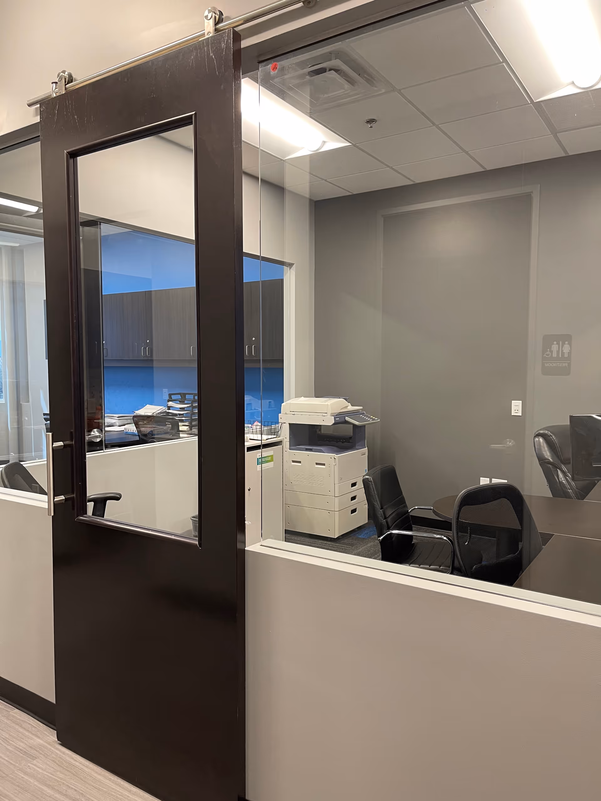 Interior office space with a glass door, copier, and chairs.