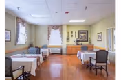 Light-filled dining room with tables covered in white cloths, upholstered chairs, and wood floors.
