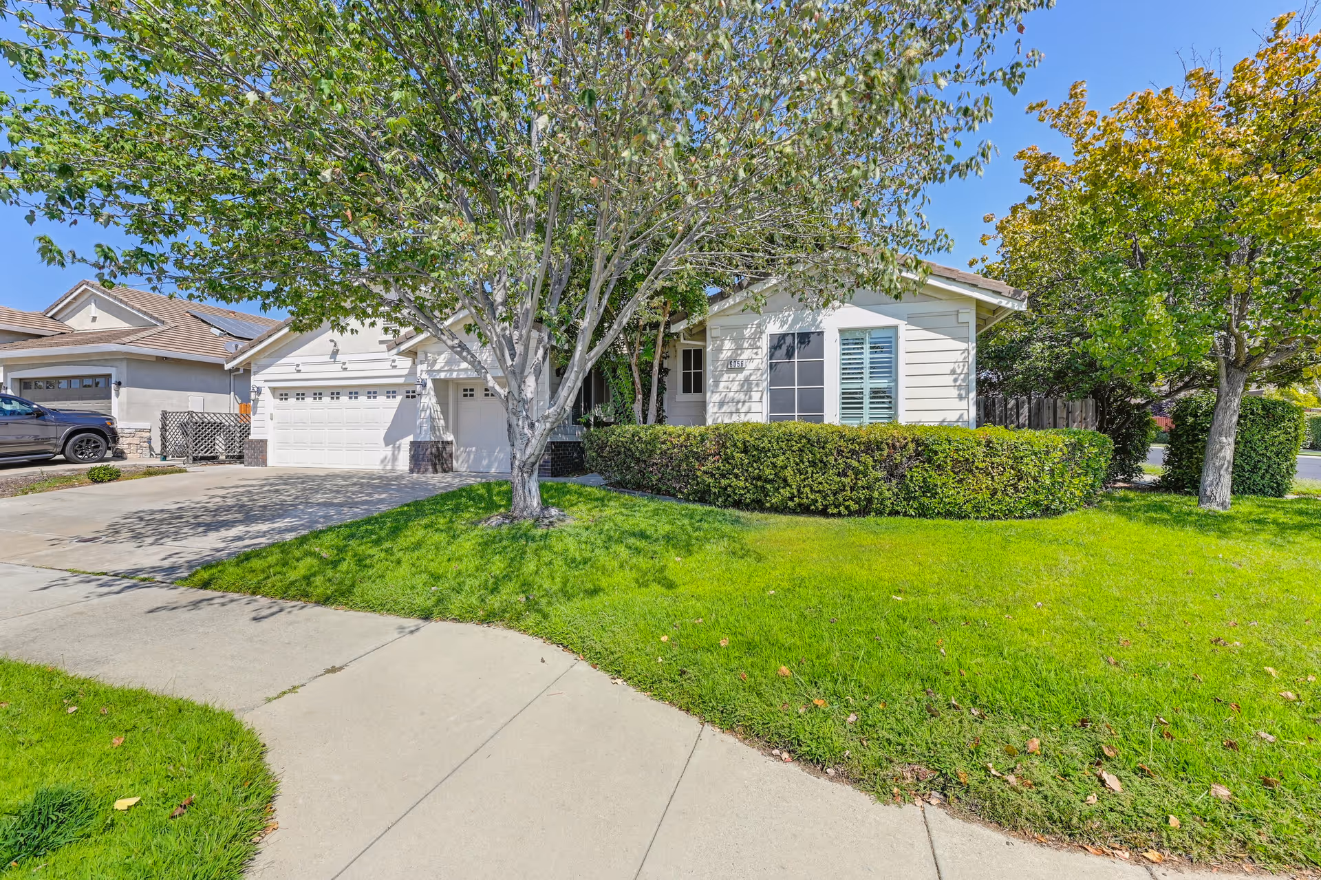 Single-story house with green lawn, trees, and curved sidewalk in a residential front yard.