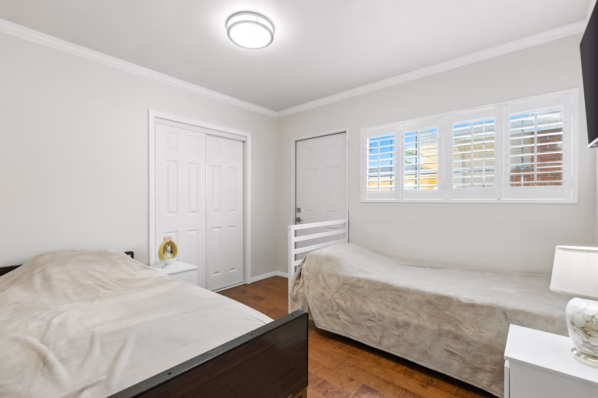 Two single beds, nightstands, and a window with blinds in a clean, neutral bedroom.
