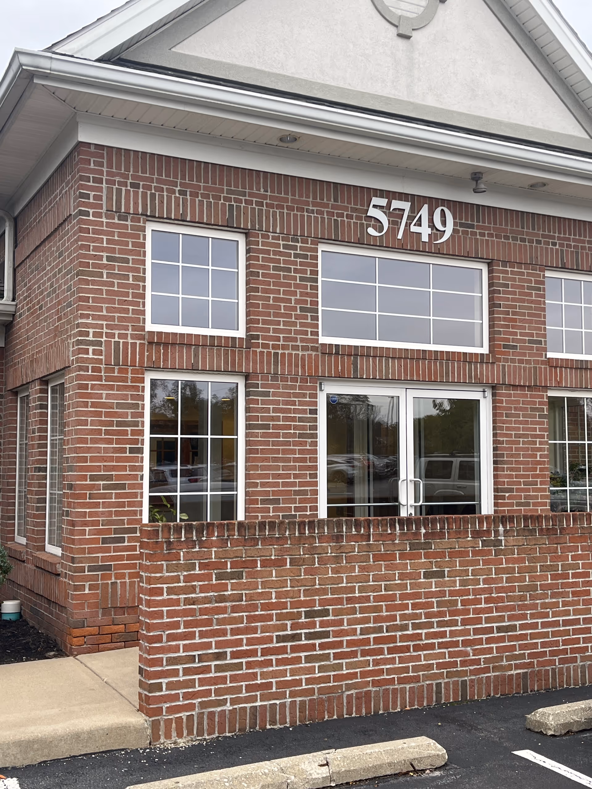 Brick building exterior with large windows, glass doors, and the address 5749 on the front.