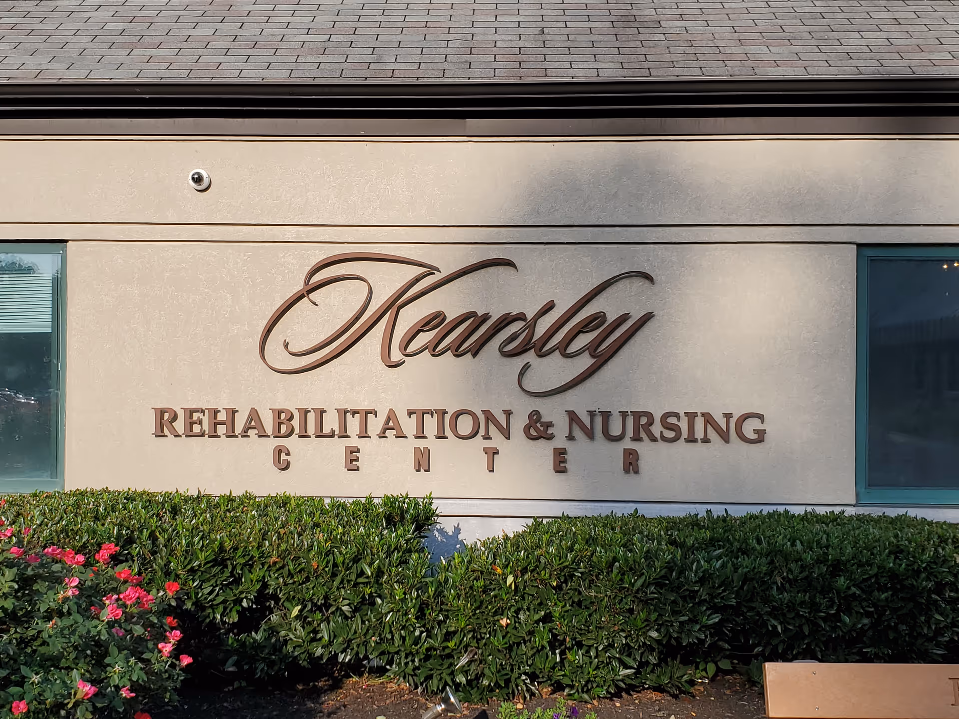 Exterior view of Kearsley Rehabilitation and Nursing Center sign with shrubs in front.