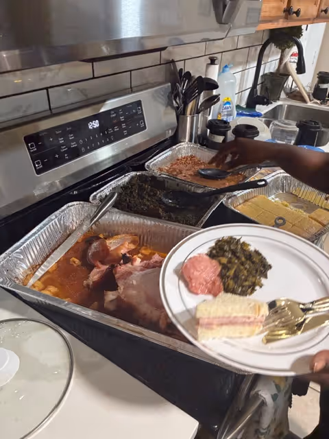 A kitchen with aluminum trays of food on a stove and a plate being served.