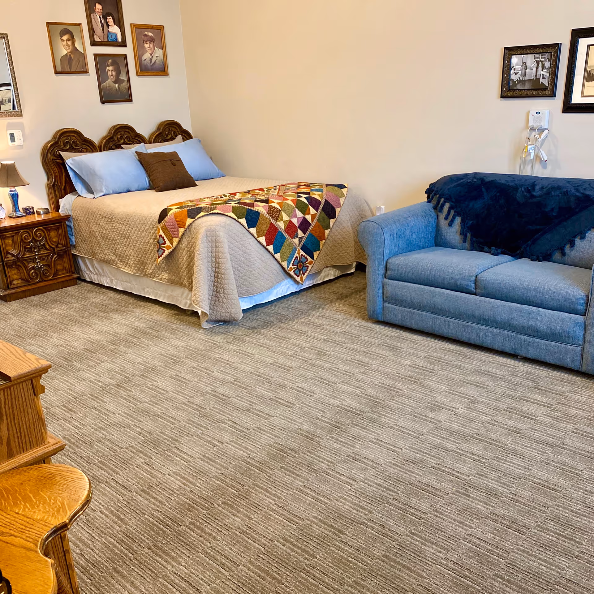 Bedroom in a senior living facility with bed, quilt, nightstand, and blue sofa.