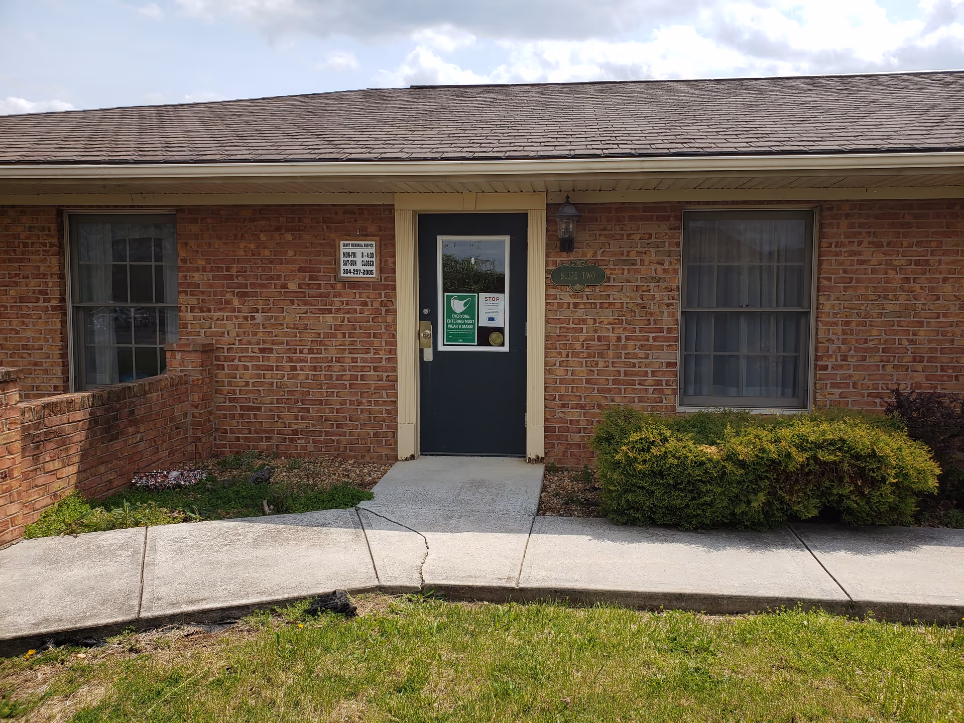 Brick exterior with central door, two windows, and trimmed shrubs.
