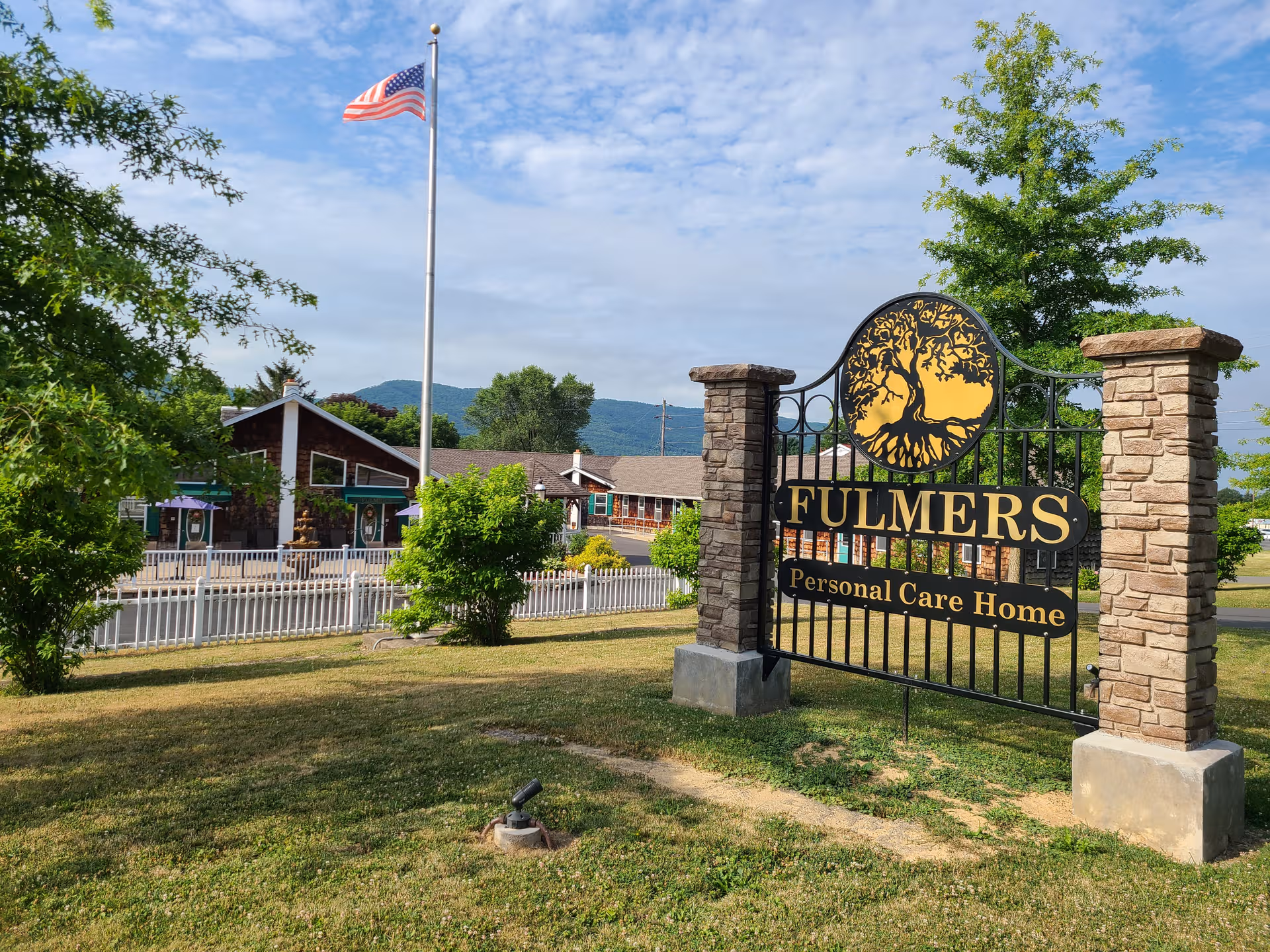 Front entrance sign for Fulmer's Personal Care Home with gate and flag.