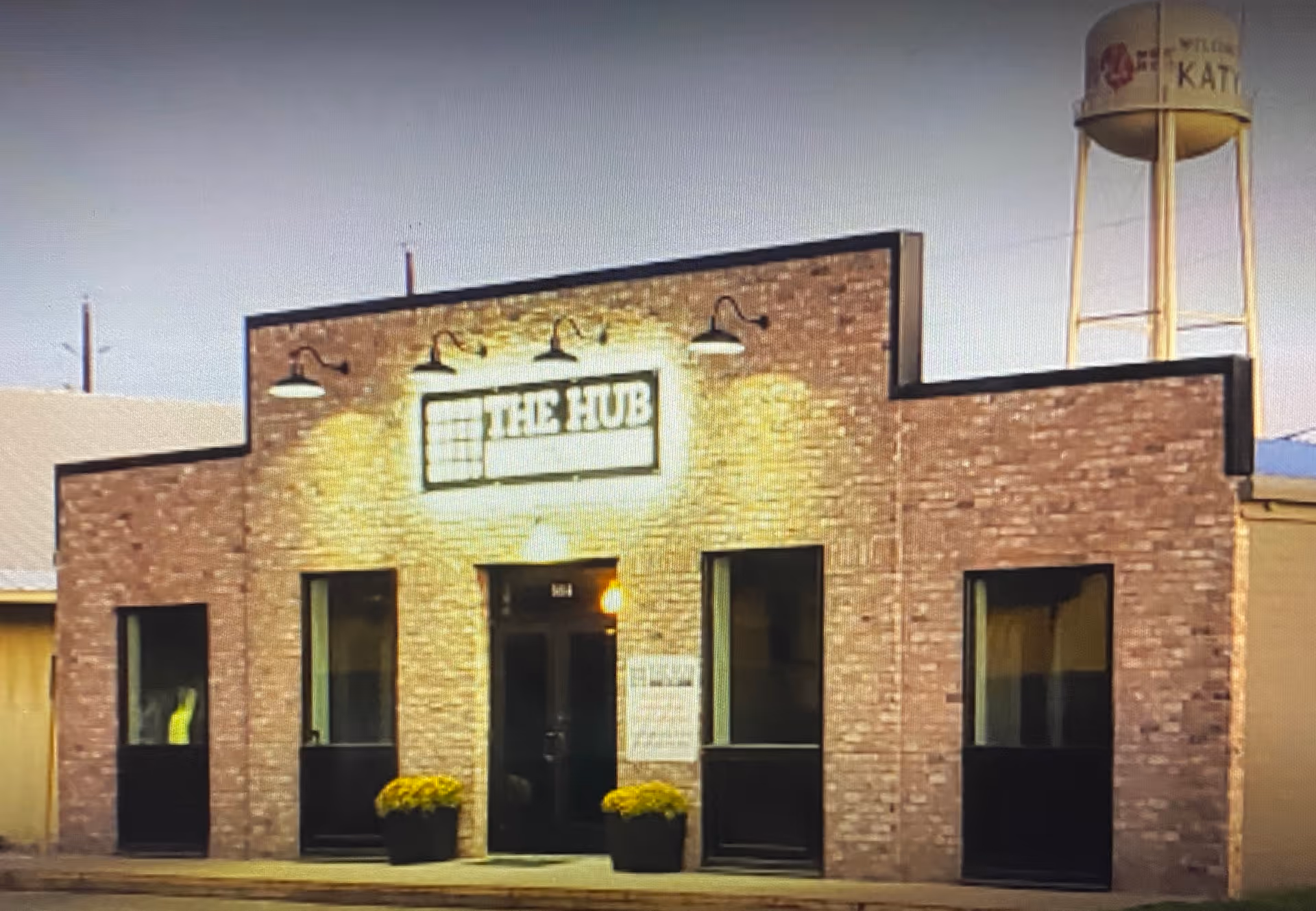 Brick-front building labeled The Hub with double doors and potted plants.