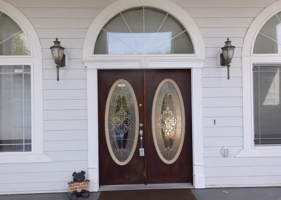 Front entrance of a light-gray building with double stained-glass doors, arched windows, and lamps.