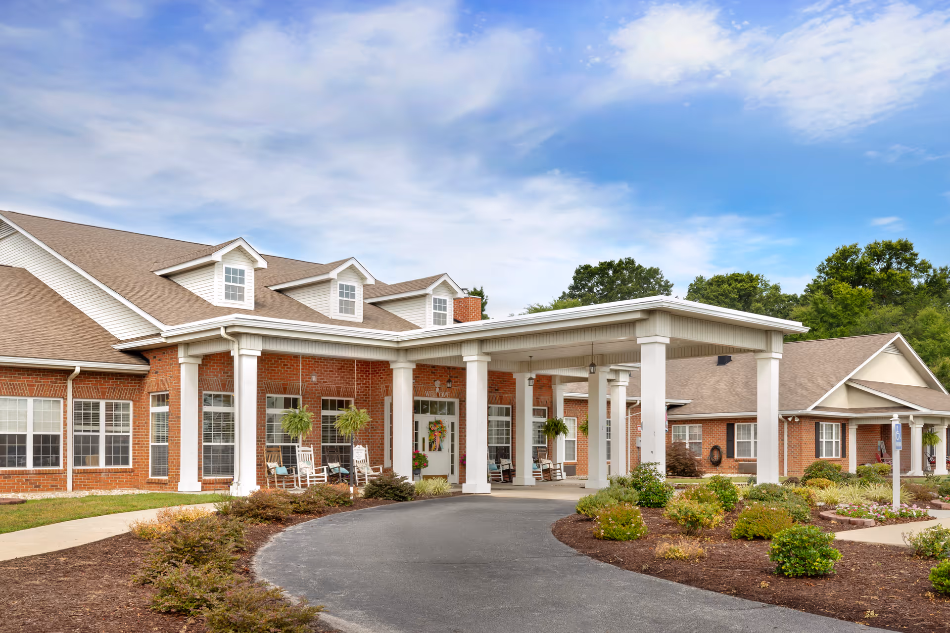 Brick senior living facility with a covered entrance and porch seating.