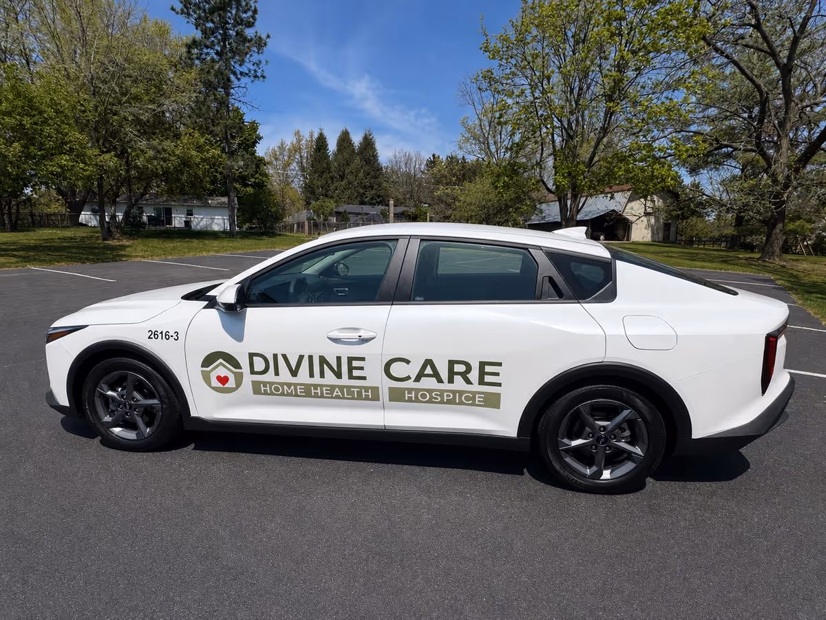White Divine Care vehicle with logo parked on a paved lot with trees in background
