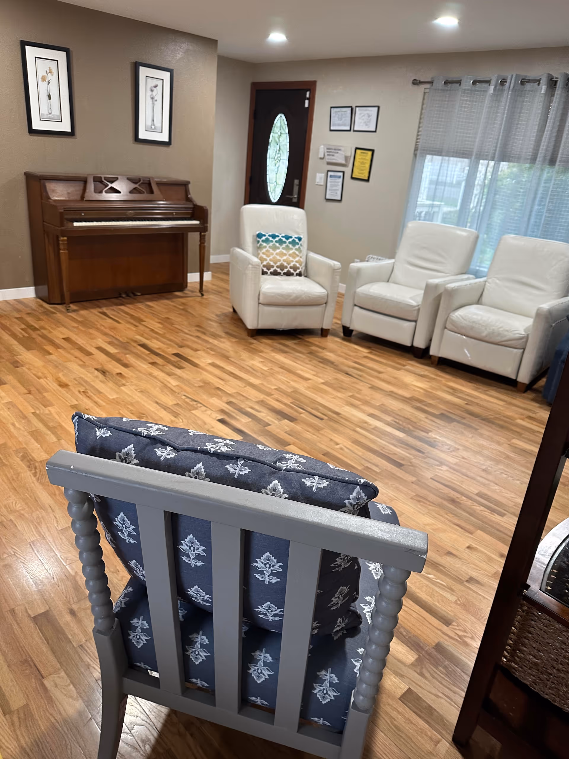 Lounge area with wood floors, white armchairs, and a piano against the wall.