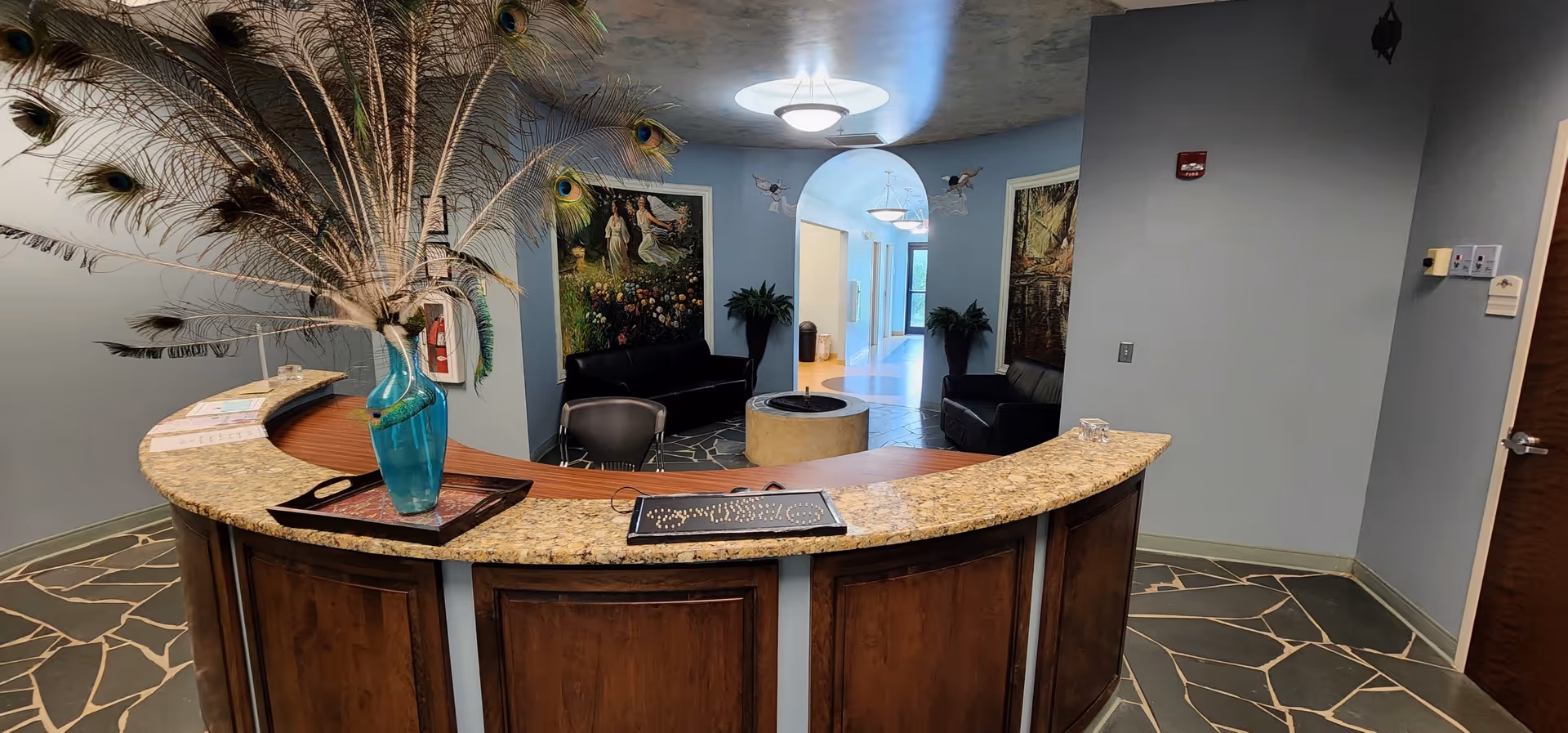 Curved granite reception desk in a blue-walled lobby with peacock feather centerpiece.