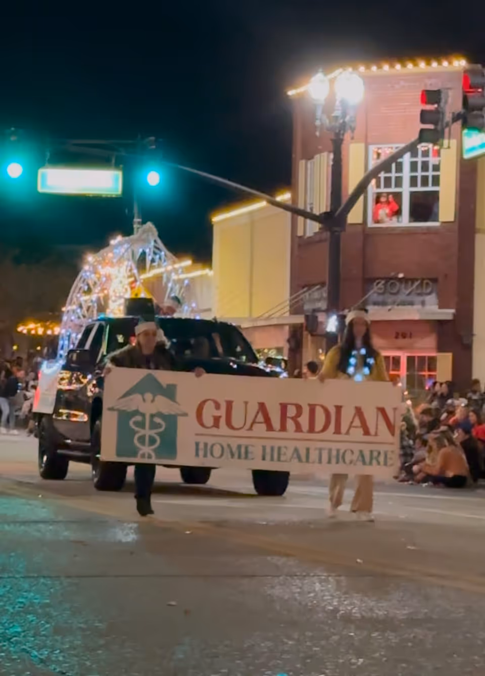 Two people walk with a Guardian Home Healthcare banner during a nighttime street parade.