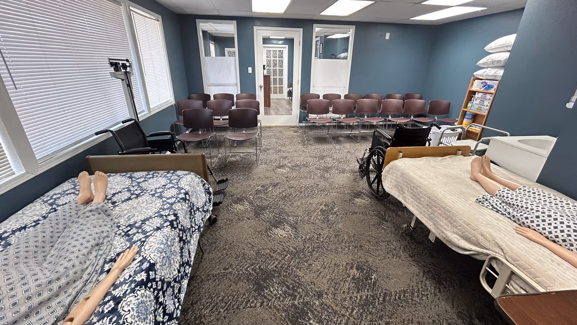 A training room inside a senior facility with two beds, wheelchairs, and rows of chairs.