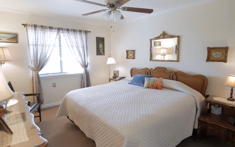 A cozy bedroom with a large bed, nightstands, lamps, window curtains, and a ceiling fan.
