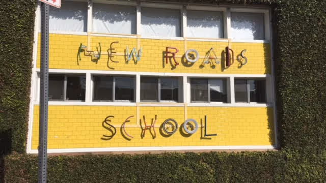 Exterior yellow-brick school building with graffiti reading New Roads School.