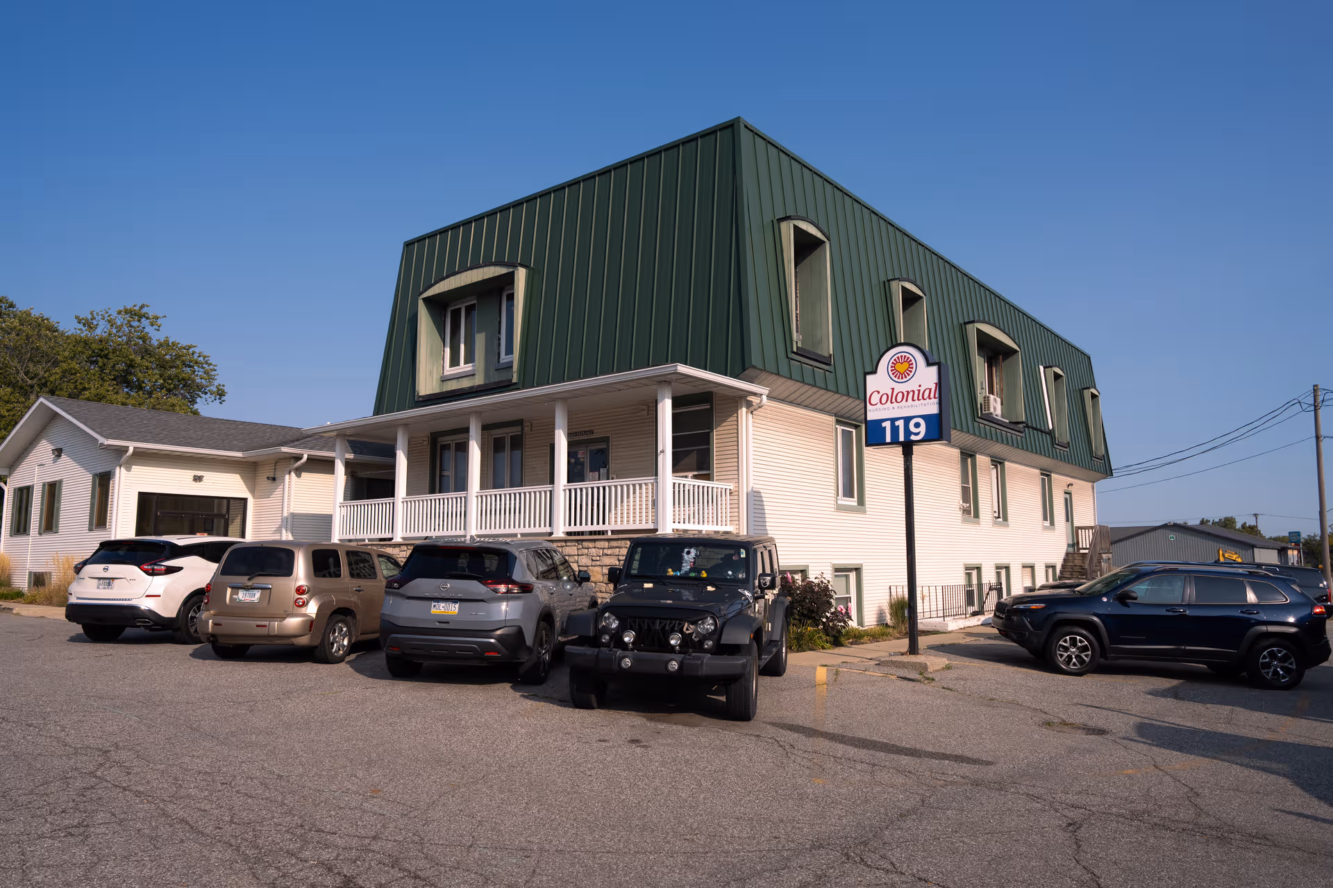 Exterior view of Colonial Nursing and Rehab building with parked cars and blue sky.