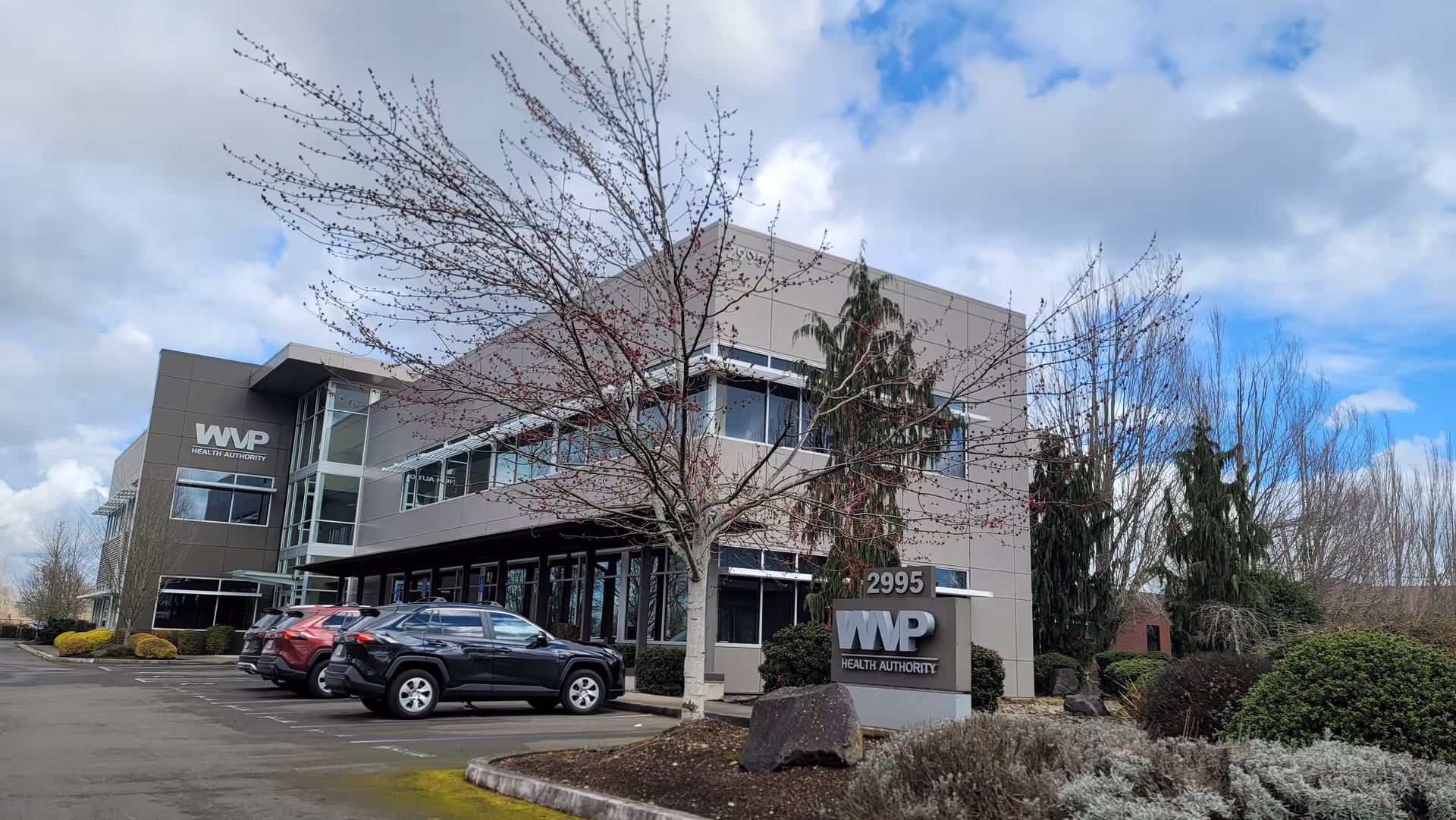 Modern two-story facility exterior with WVP Health Authority sign and parked cars.