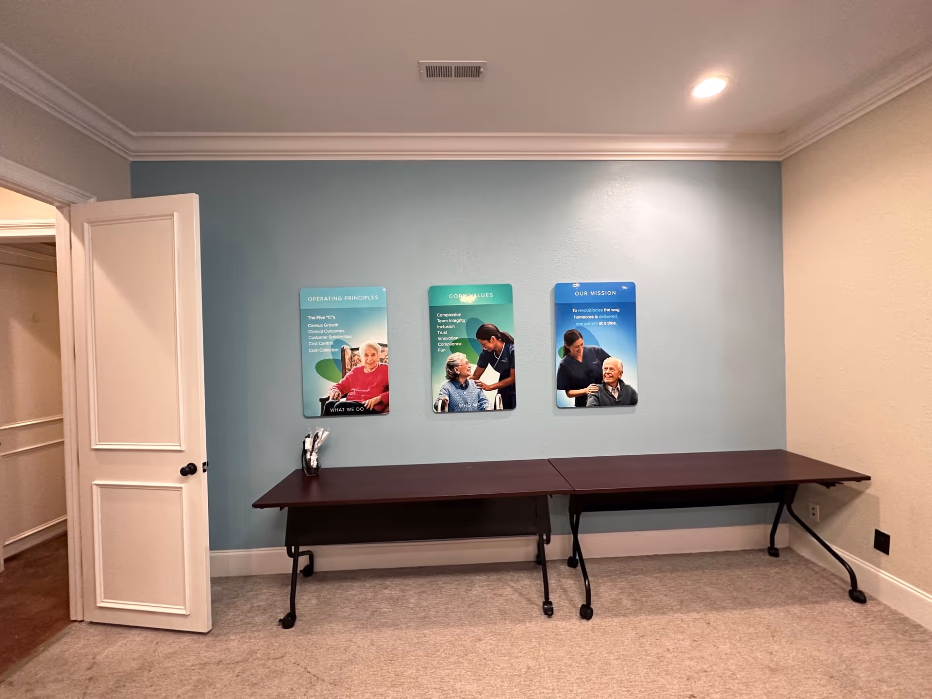 A long table against a blue wall with three posters and a doorway on the left.