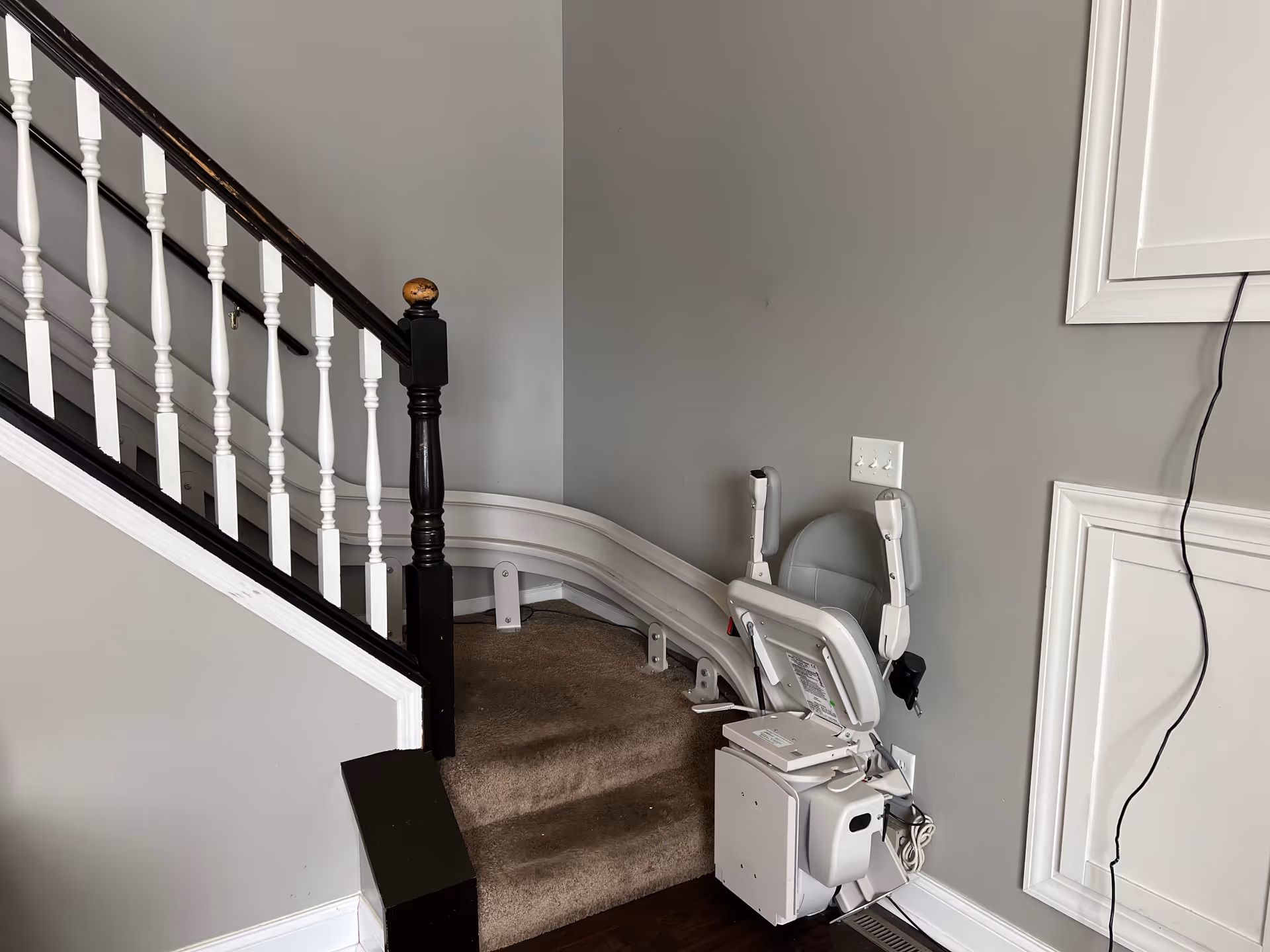 Indoor staircase with a wall-mounted chair lift, white railings, and gray walls.