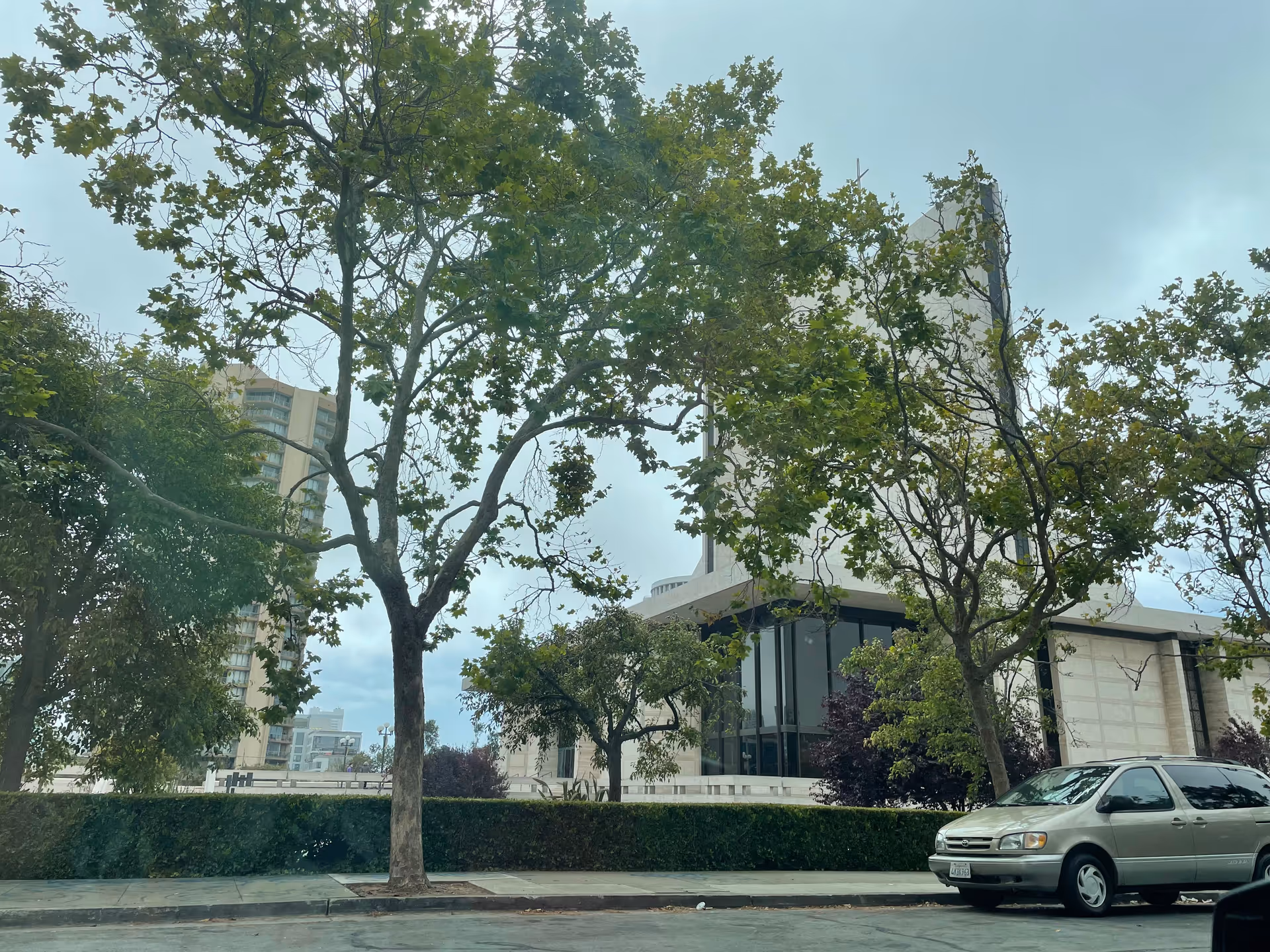 Exterior of a modern senior living building framed by trees and a parked minivan.