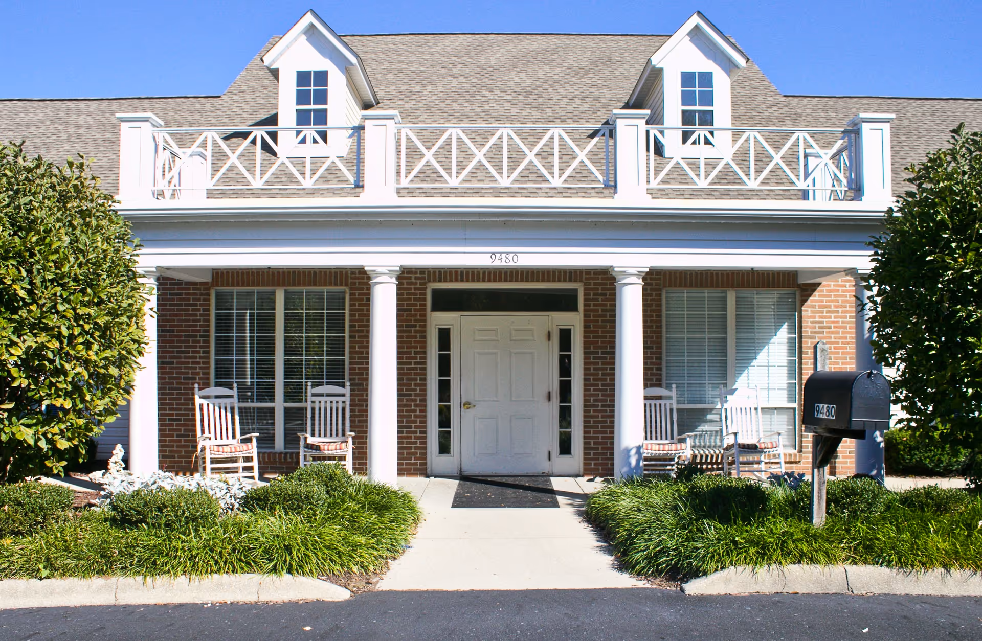 Front view of a brick senior living building with white columns, balconies, and a mailbox.