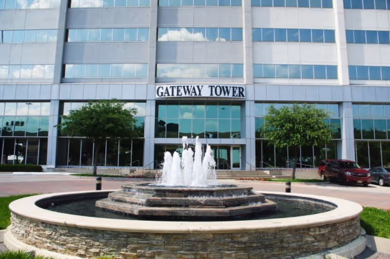 Glass-fronted Gateway Tower building with a circular fountain and trees in front