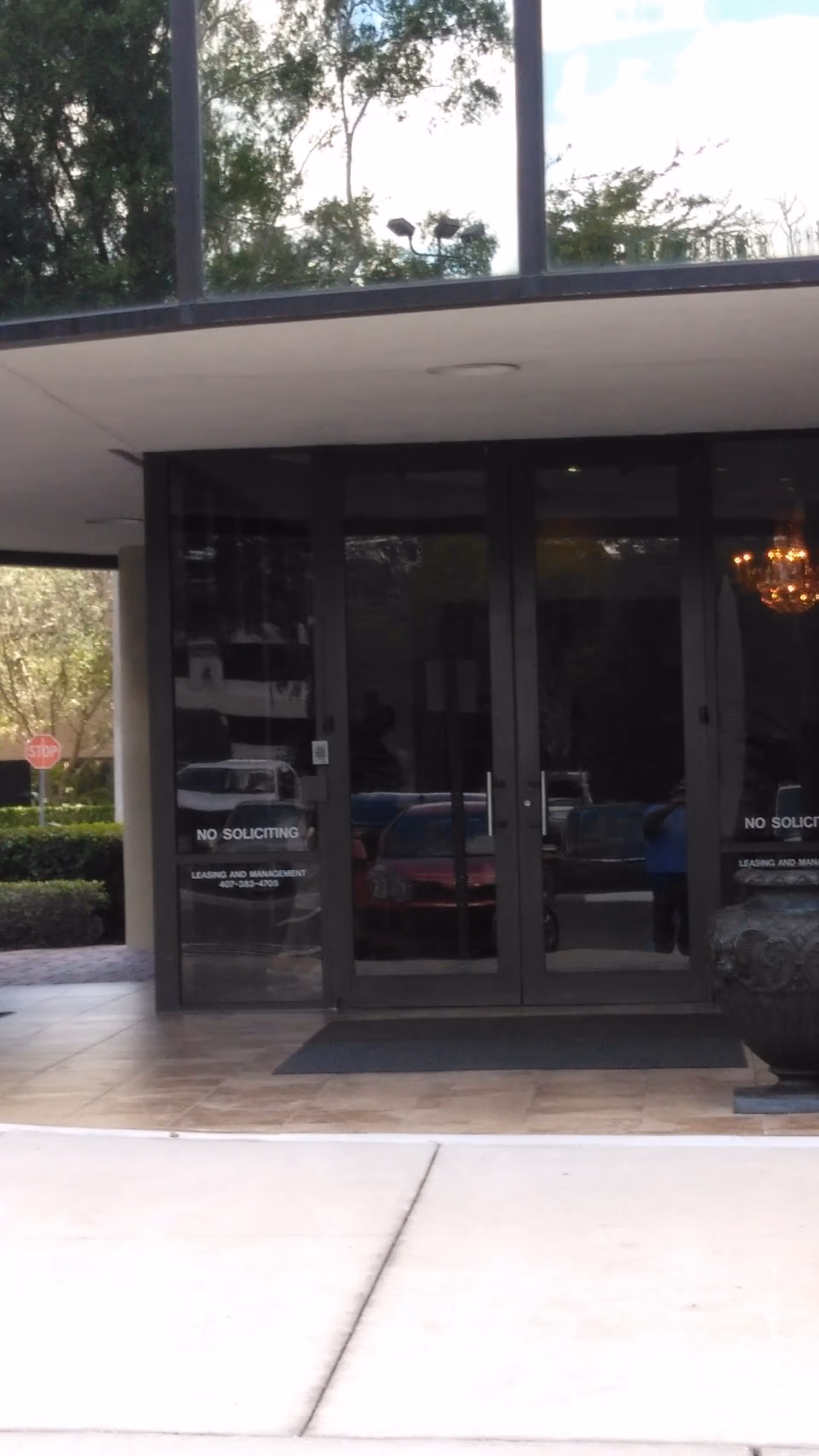 Front glass entrance of a modern building with dark doors and reflections.