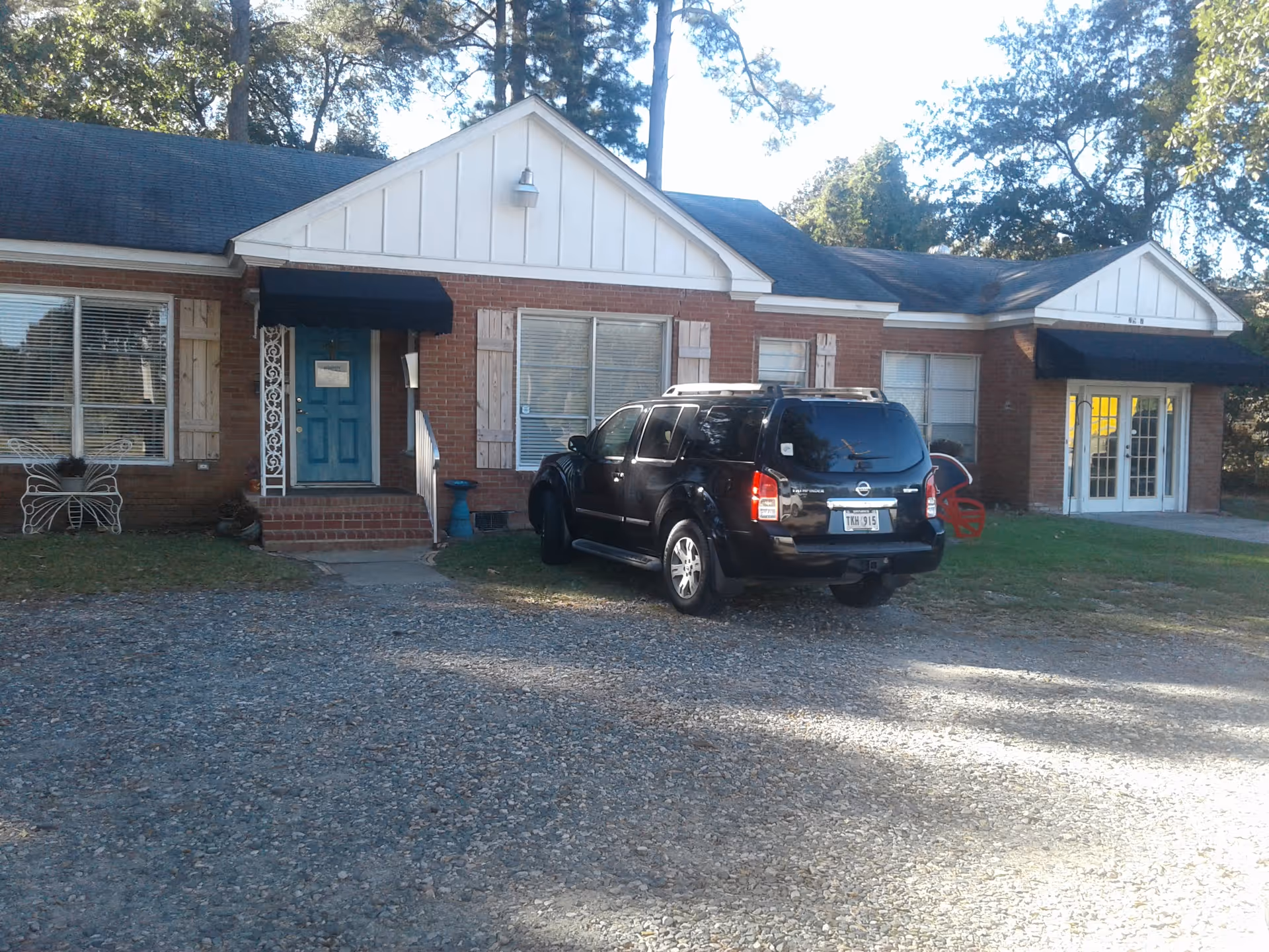 Brick senior living facility exterior with blue doors and a parked SUV in gravel driveway
