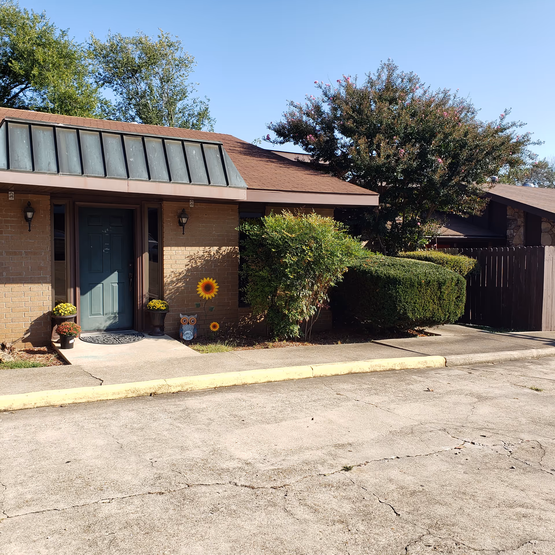 Brick senior living facility entrance with plants and sunflowers by the door.