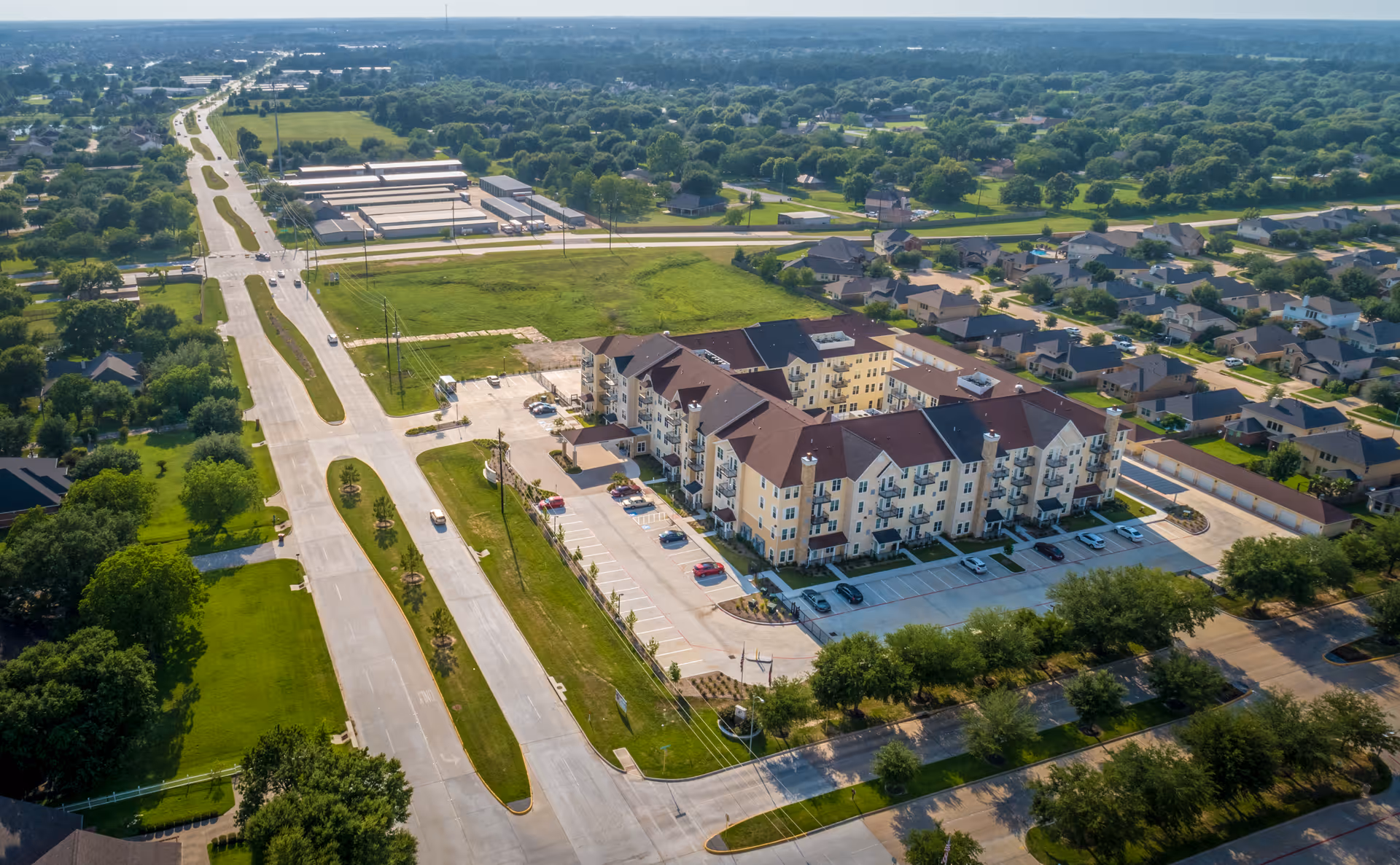 Aerial view of a multi-story retirement apartment complex with parking lots, surrounding streets, and nearby houses.