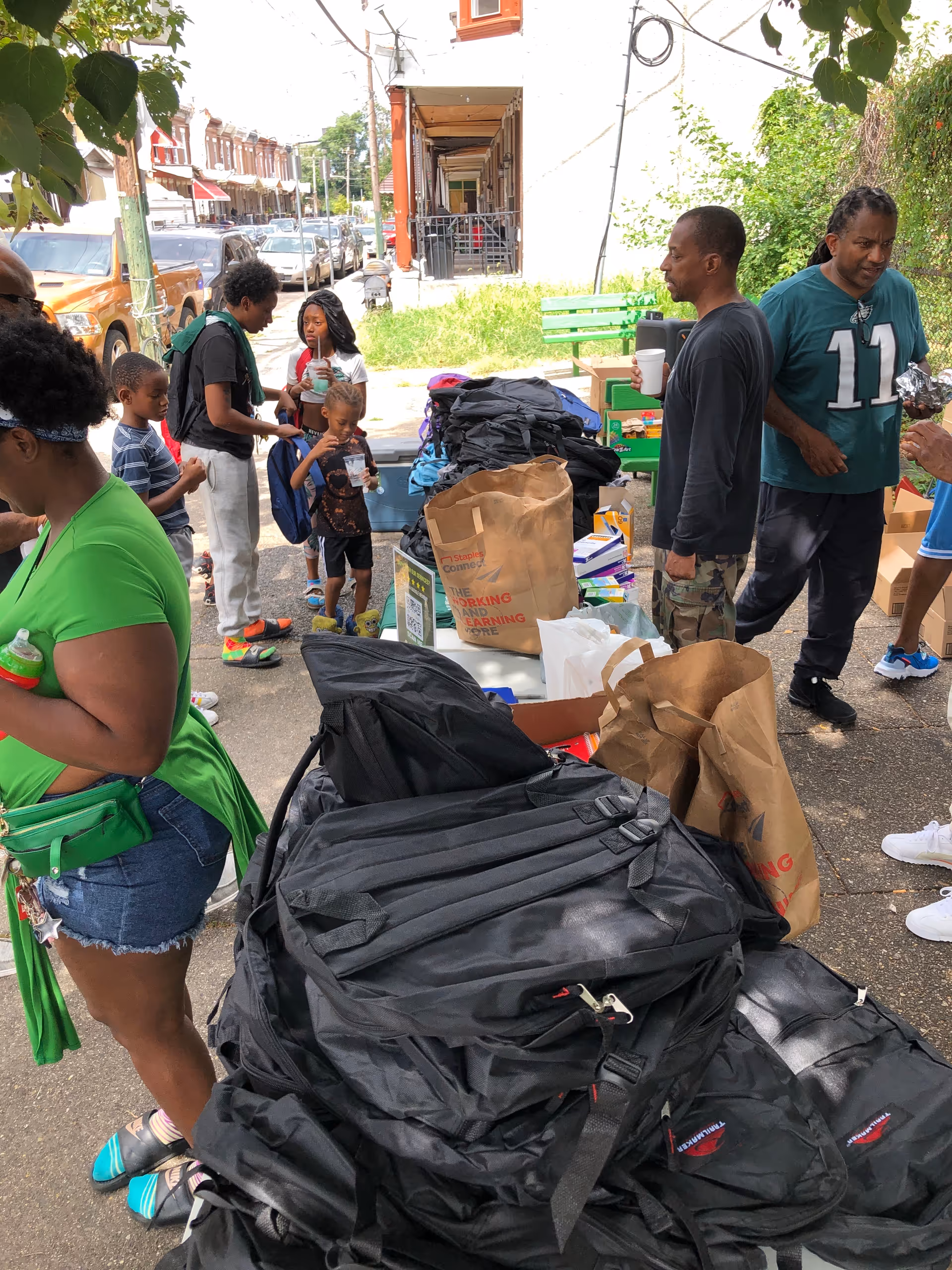 People gather on a street with bags and supplies outside a building.