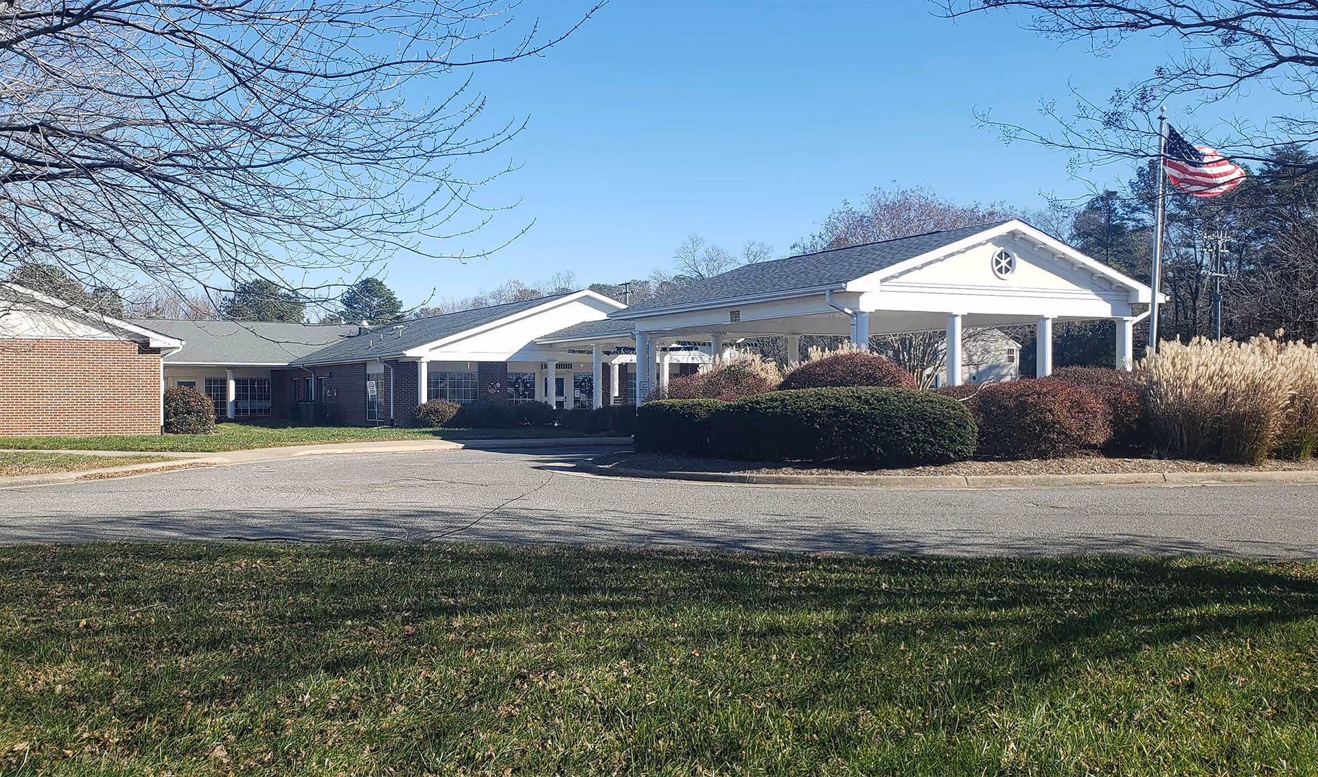 Exterior view of a senior living facility entrance with a covered drop-off area and flag.