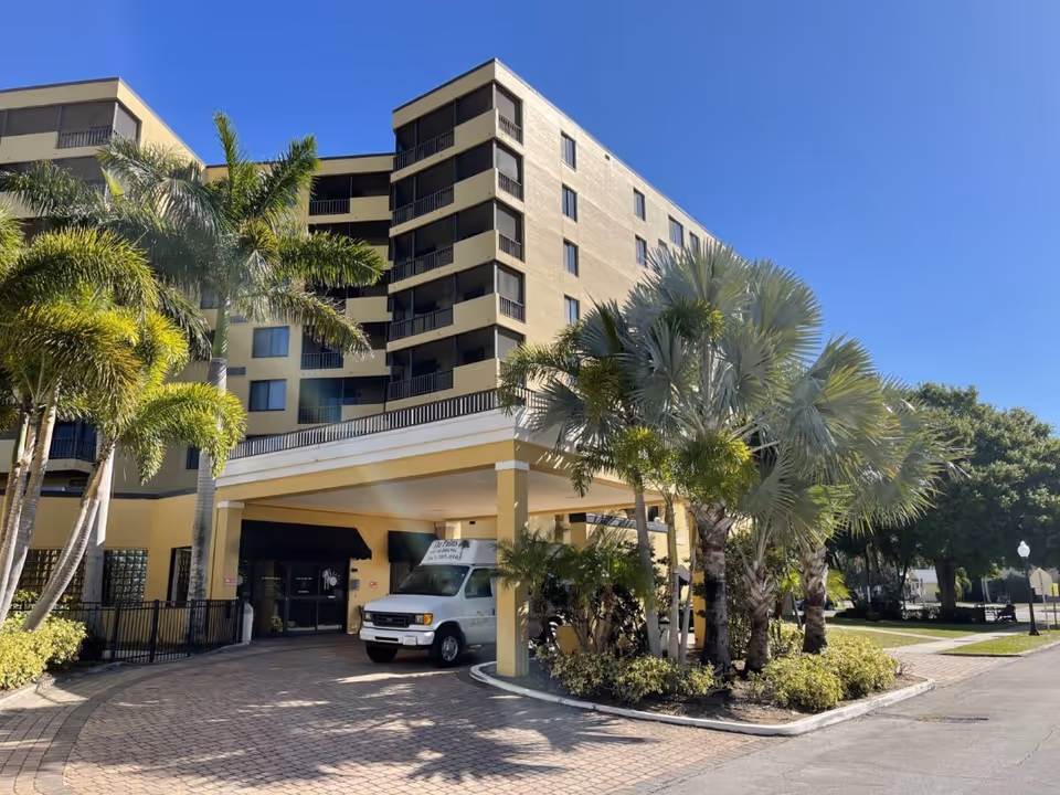Exterior view of The Palms at Sebring, a multi-story senior living building with palm trees.