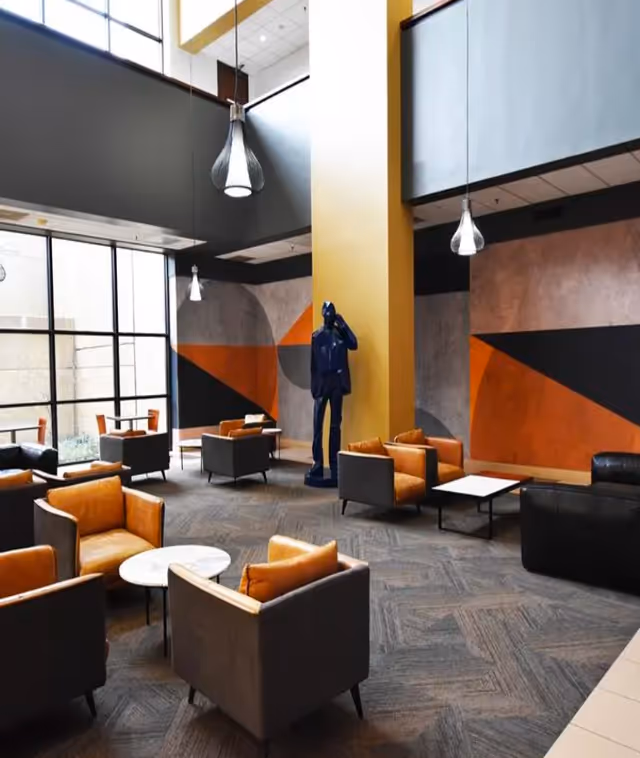 Modern lounge with orange-gray seating, round tables, and geometric wall decor.