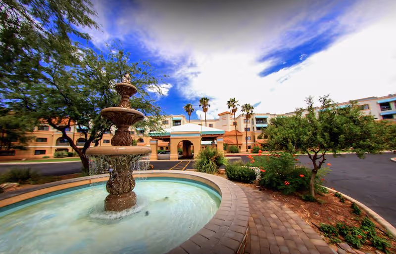 Outdoor courtyard with a tiered fountain, brick walkway, and The Forum at Tucson building.