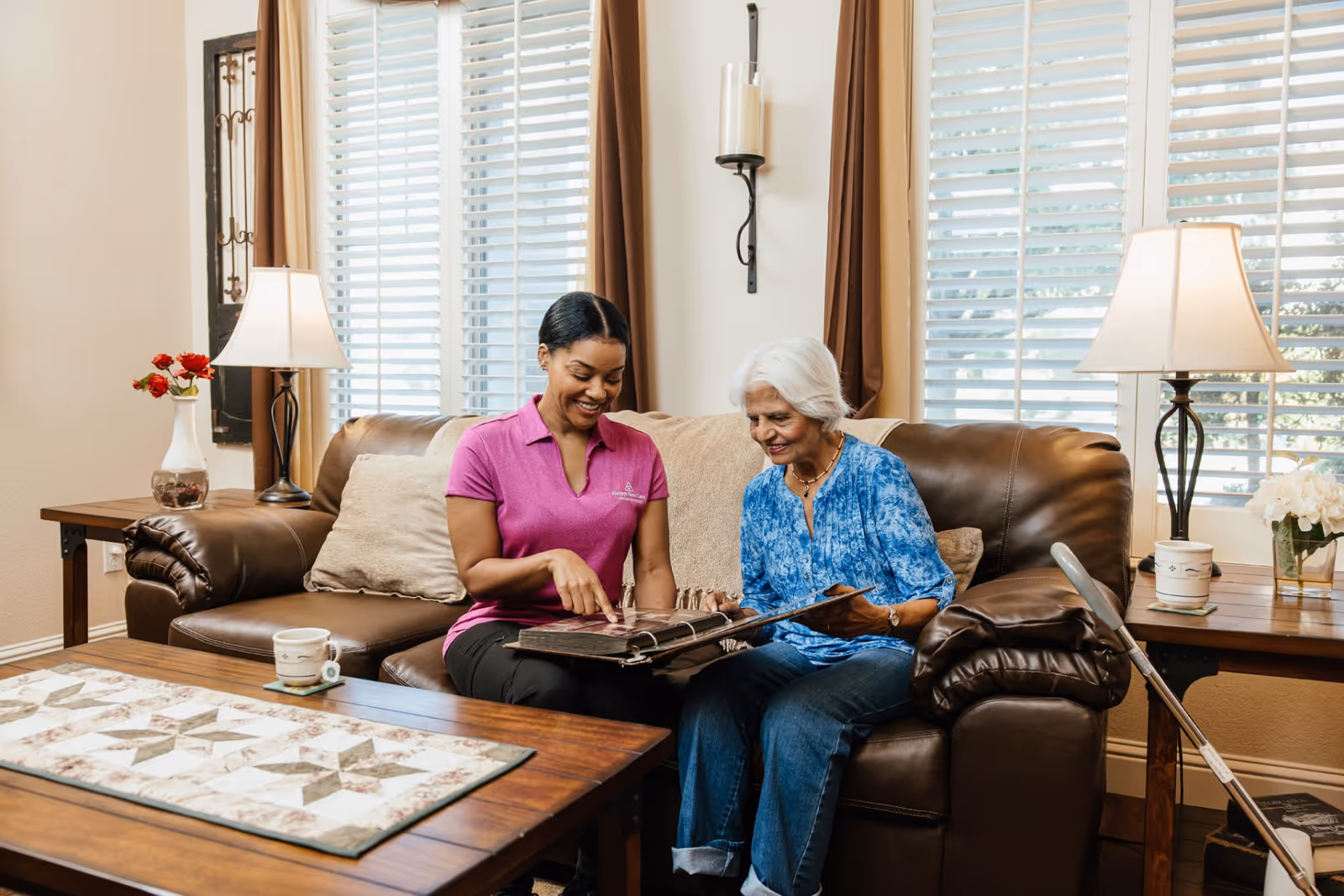Caregiver and elderly resident examine a photo album in a cozy living room.