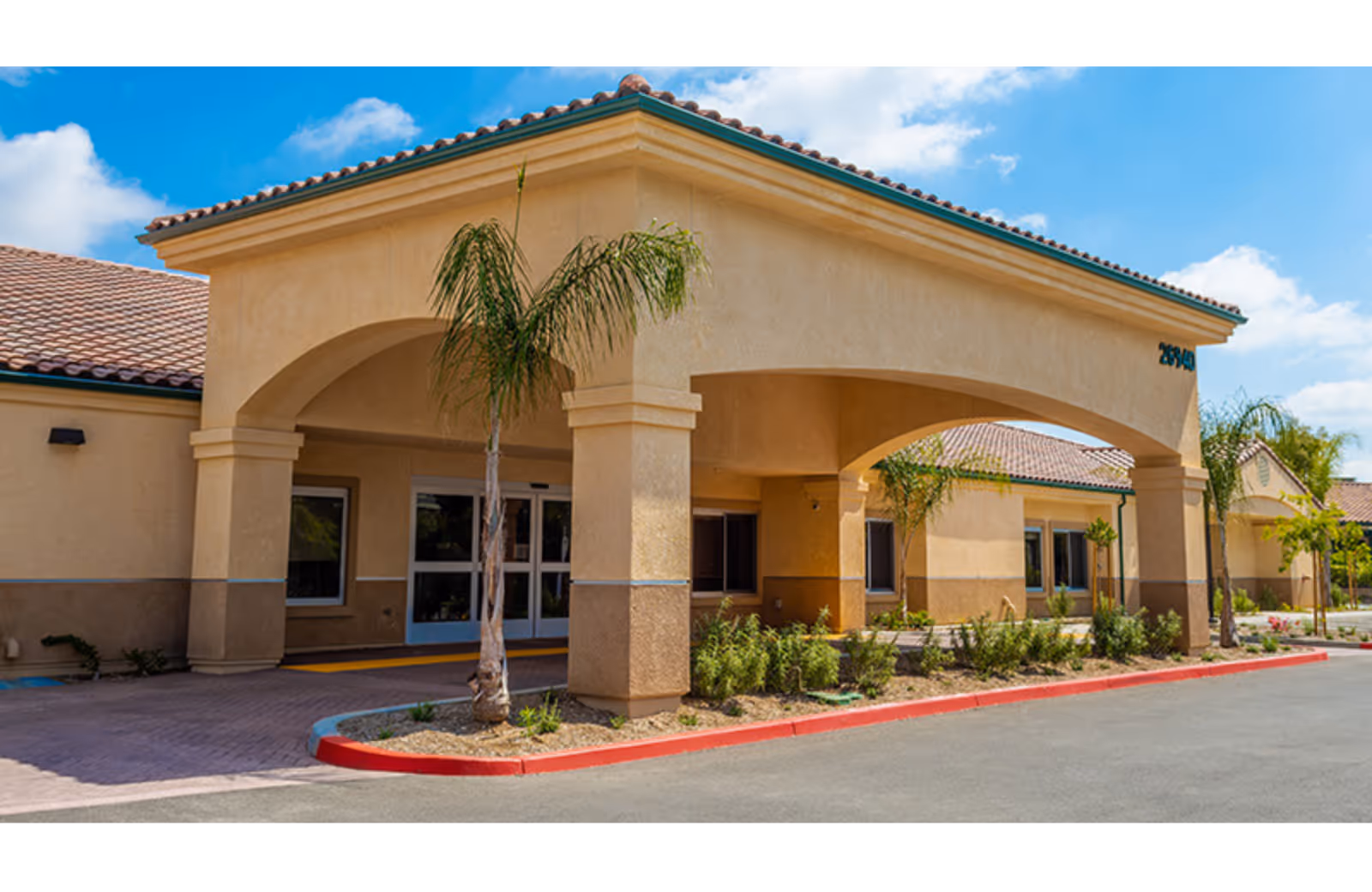 Exterior view of a beige Rancho Bellagio Post Acute building with arches and palm trees.
