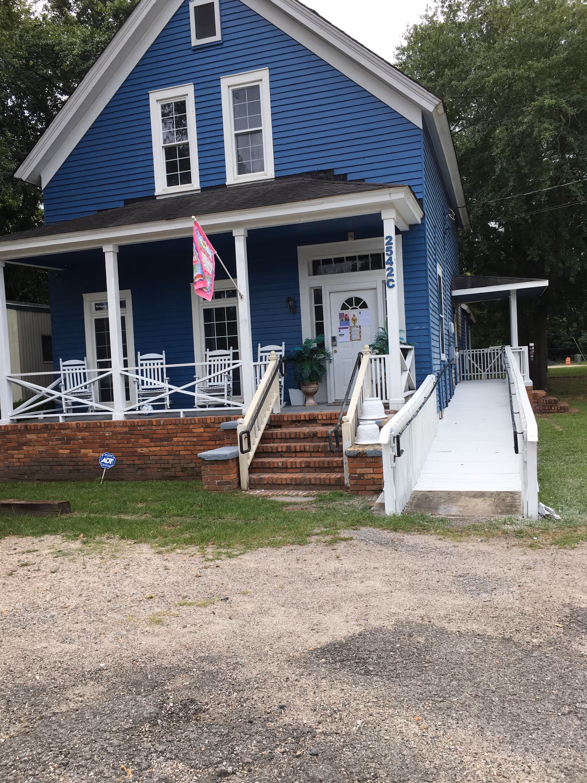 Blue two-story senior care home front with white porch, stairs, and ramp.