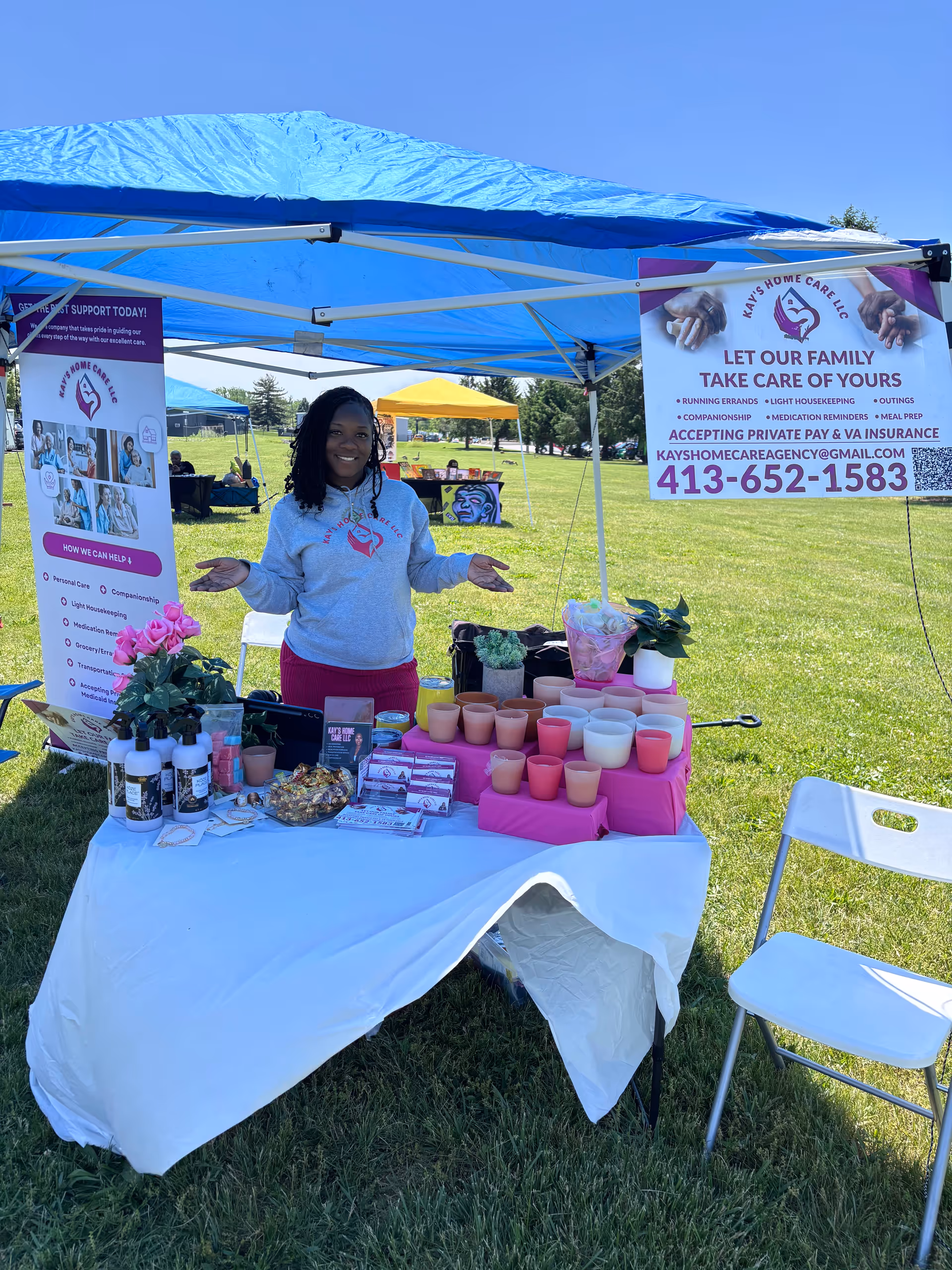Smiling staff member at Kay's Home Care LLC booth under a blue outdoor canopy.