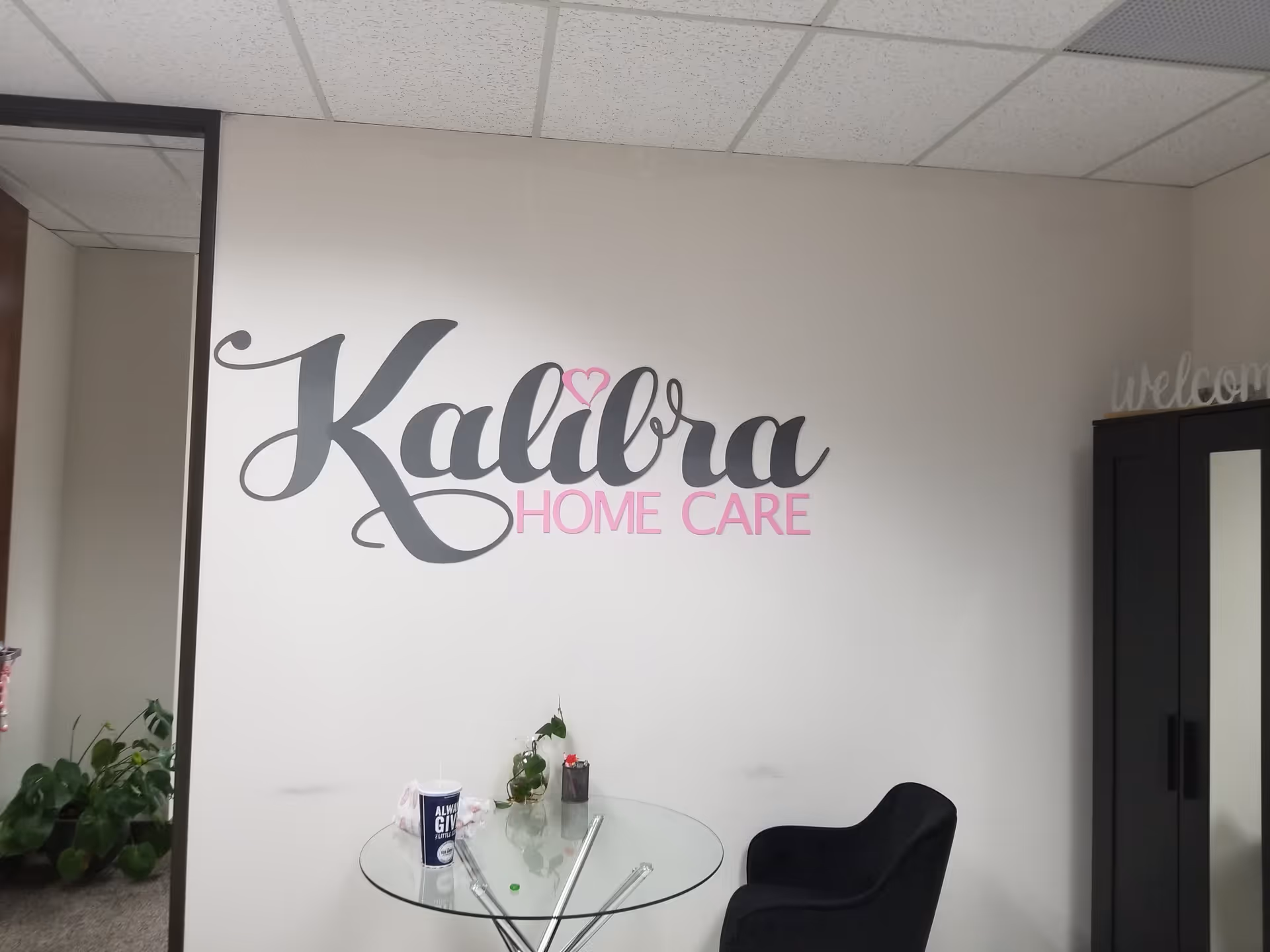 Interior lobby area with Kalibra Home Care logo on the wall and a glass table.