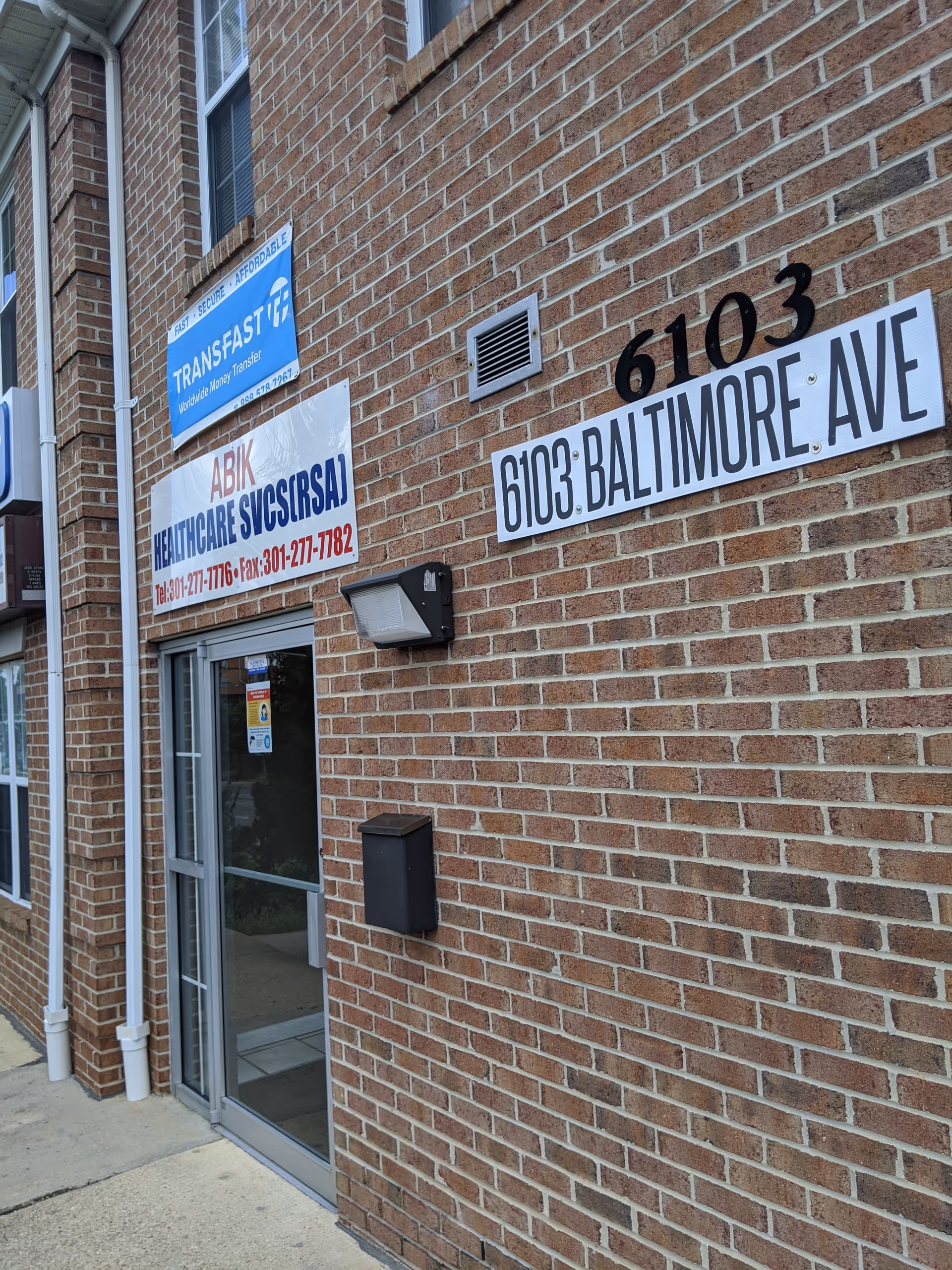 Brick building exterior with entrance and signs reading 6103 Baltimore Ave.