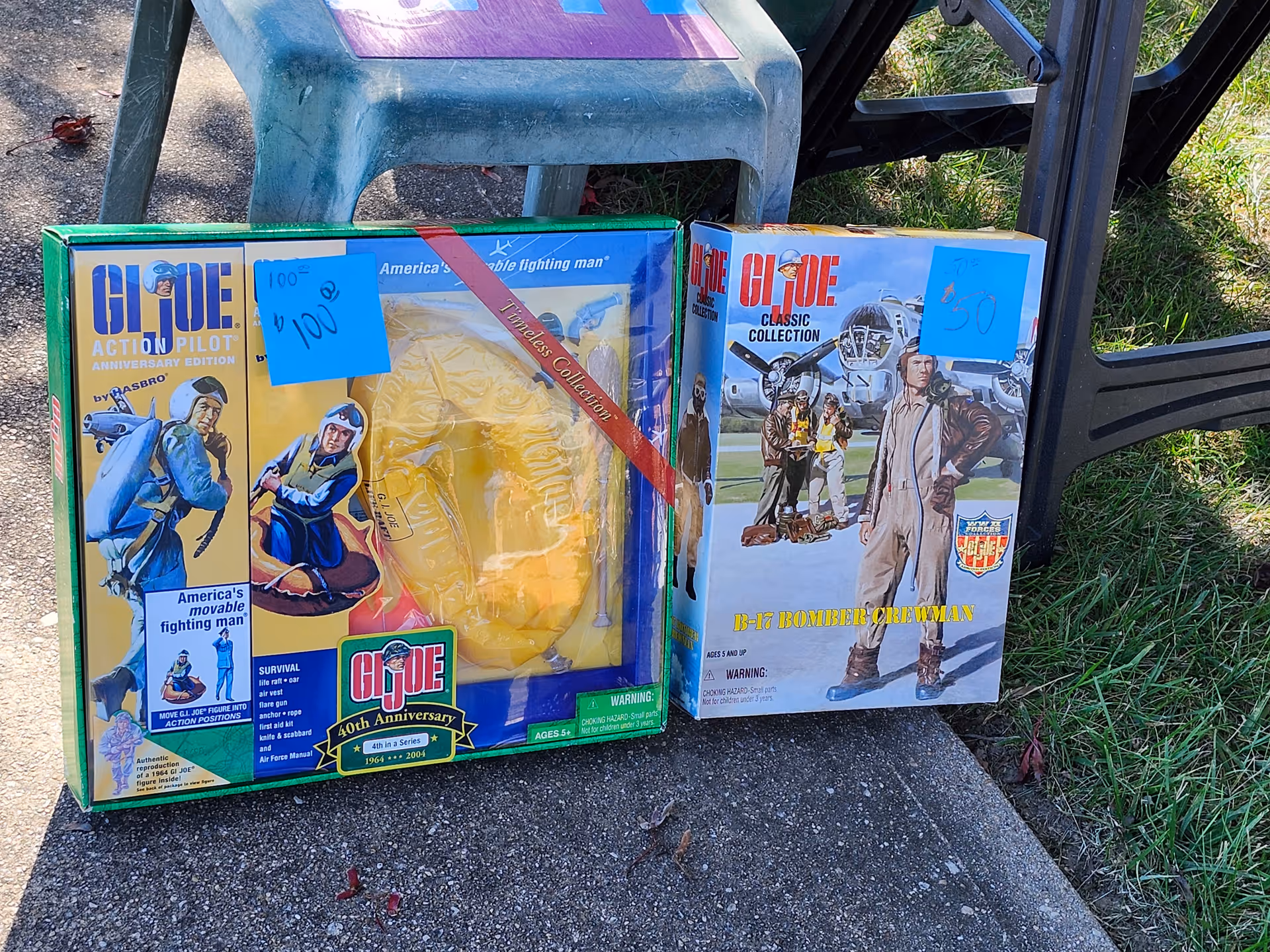 Two G.I. Joe action figure boxes on the ground beside a plastic chair outdoors.