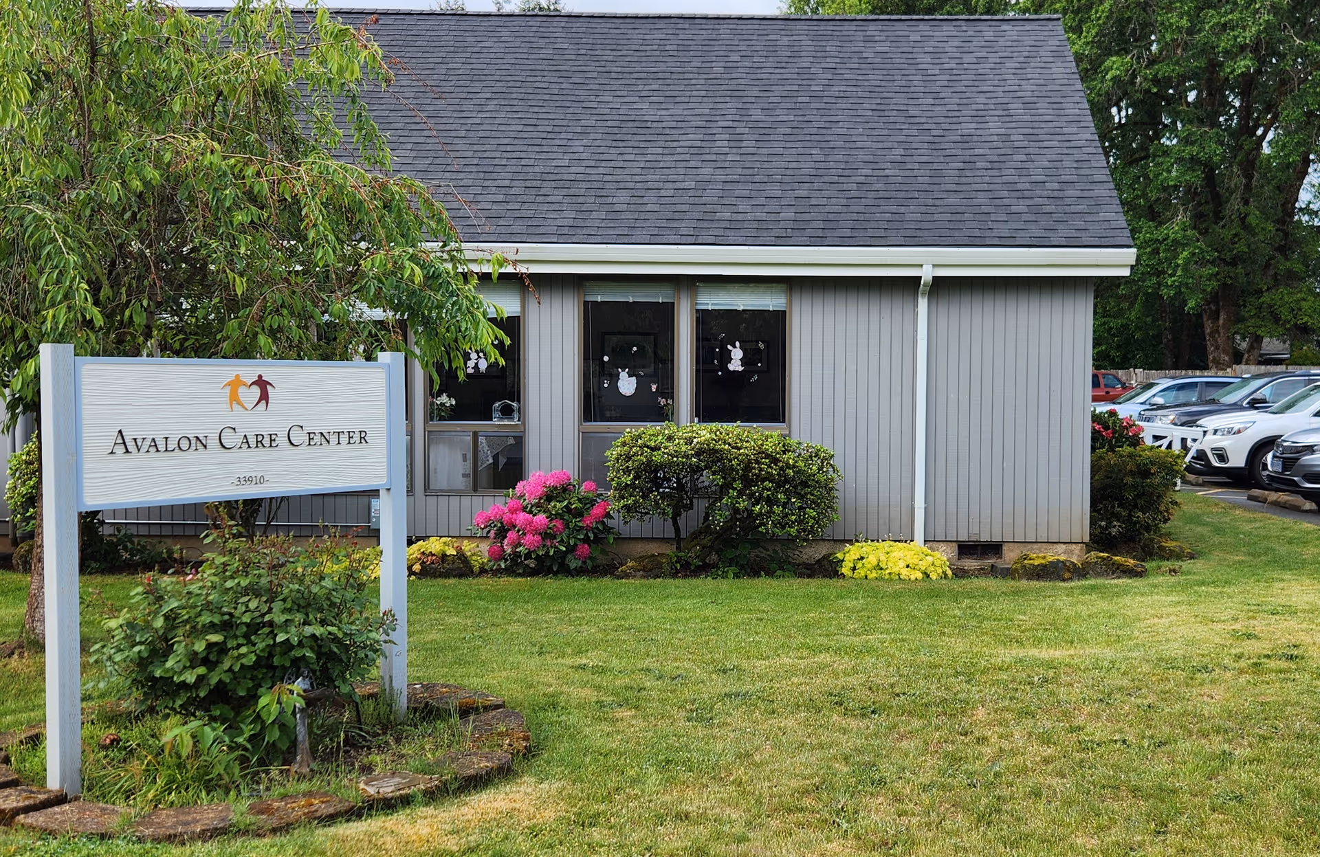 Small gray single-story building with landscaping and a sign in the lawn that reads "Avalon Care Center".