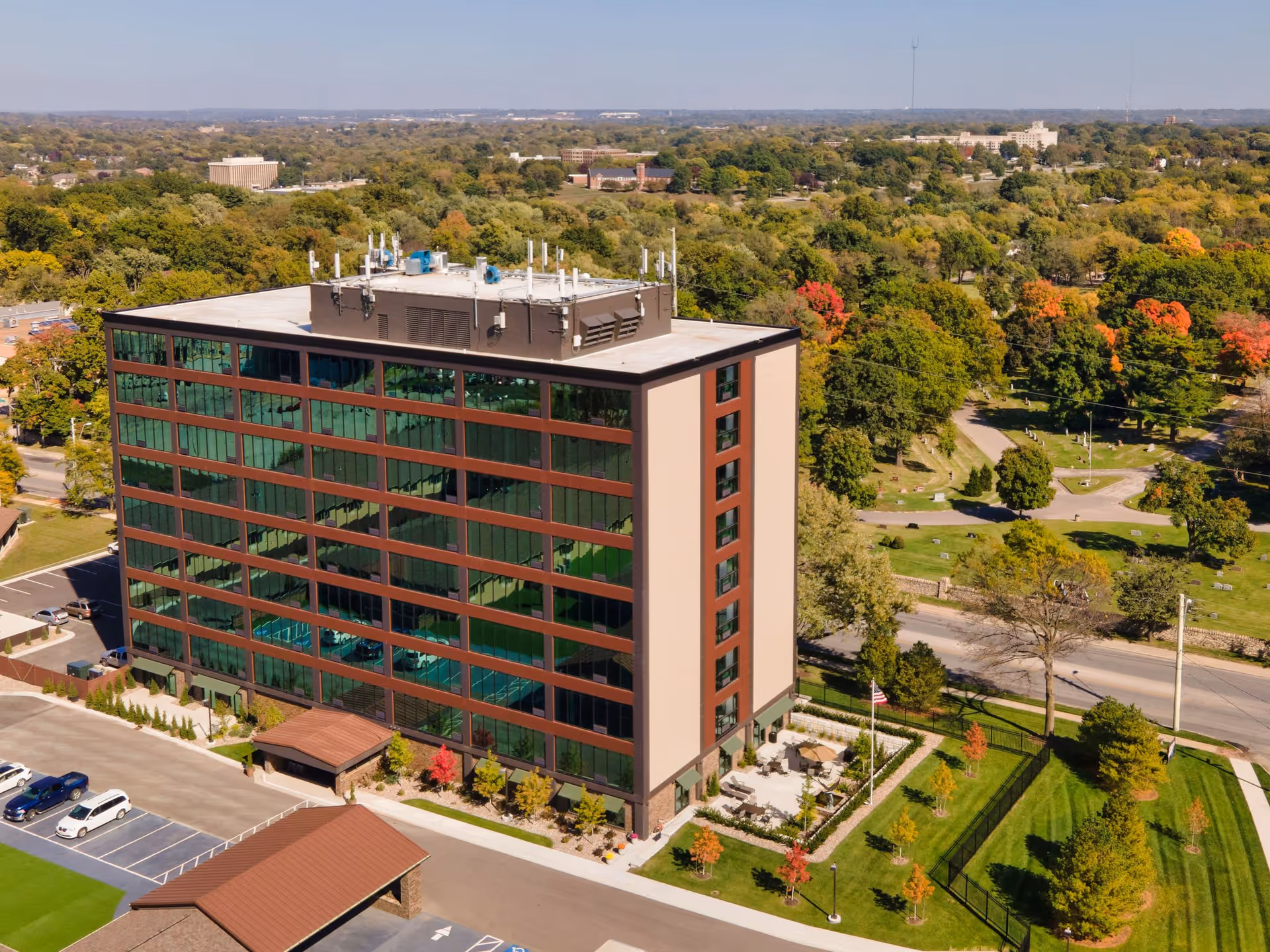 Aerial view of a multi-story senior living building with glass windows, parking lot and landscaped grounds.
