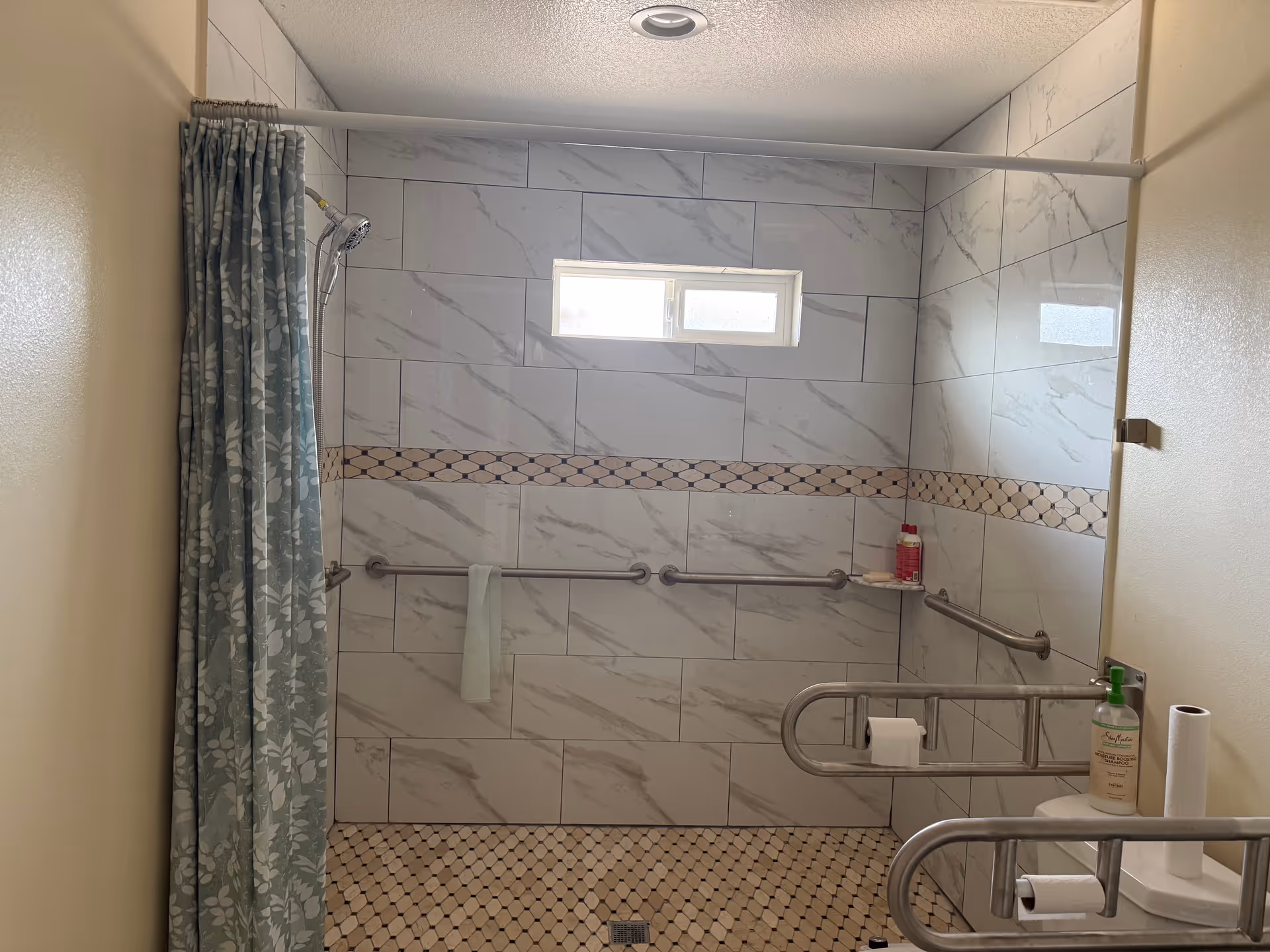 Accessible bathroom with tiled walls, grab bars, a shower curtain, and a small window.