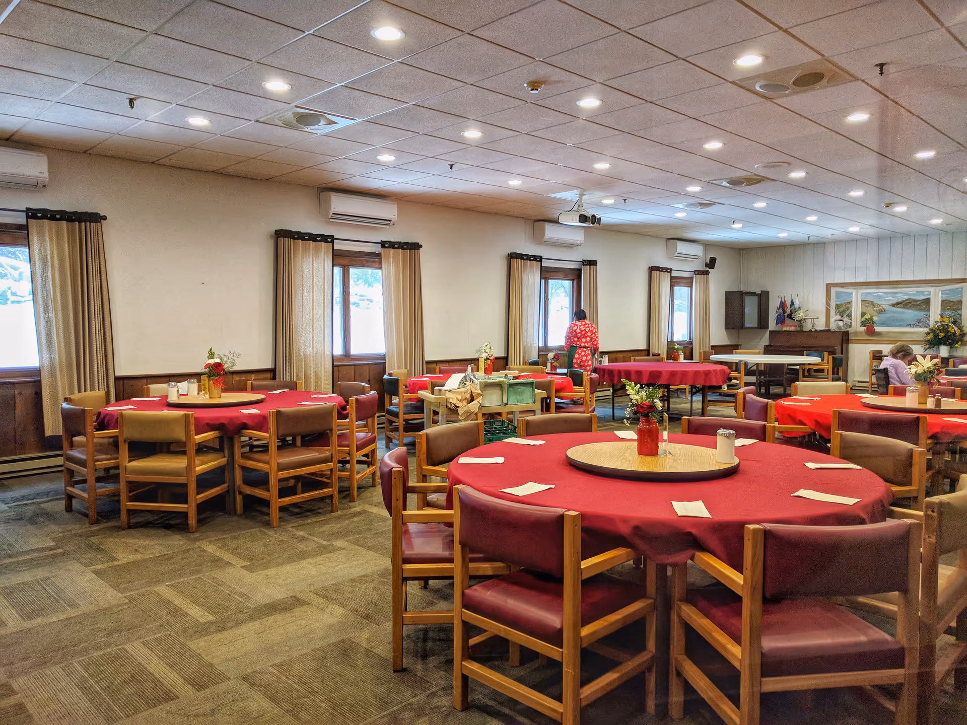Dining hall at New Windsor Country Inn with round tables, red cloths, and windows.