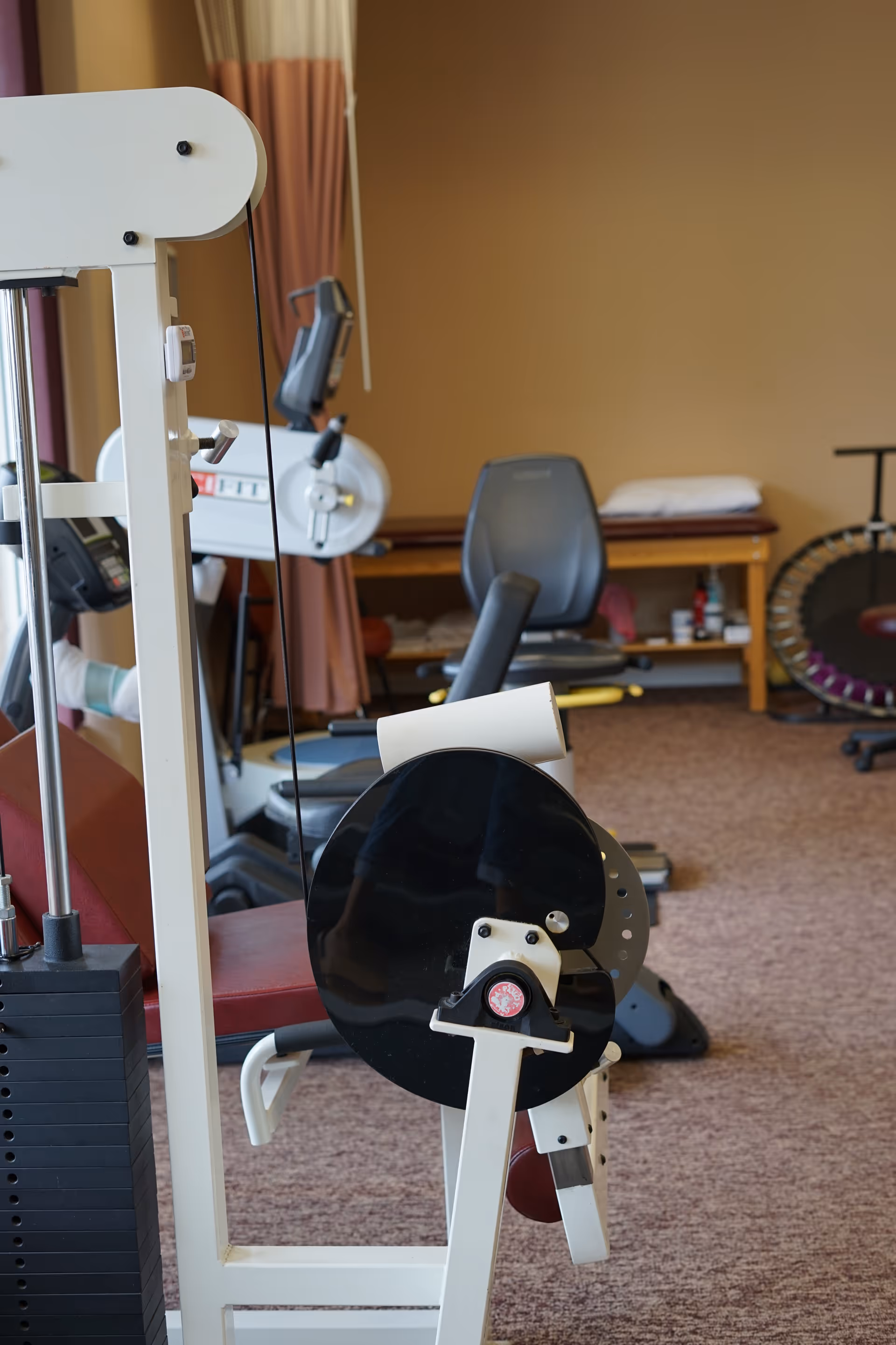 Interior rehab room with exercise machines, a chair, and a bed.