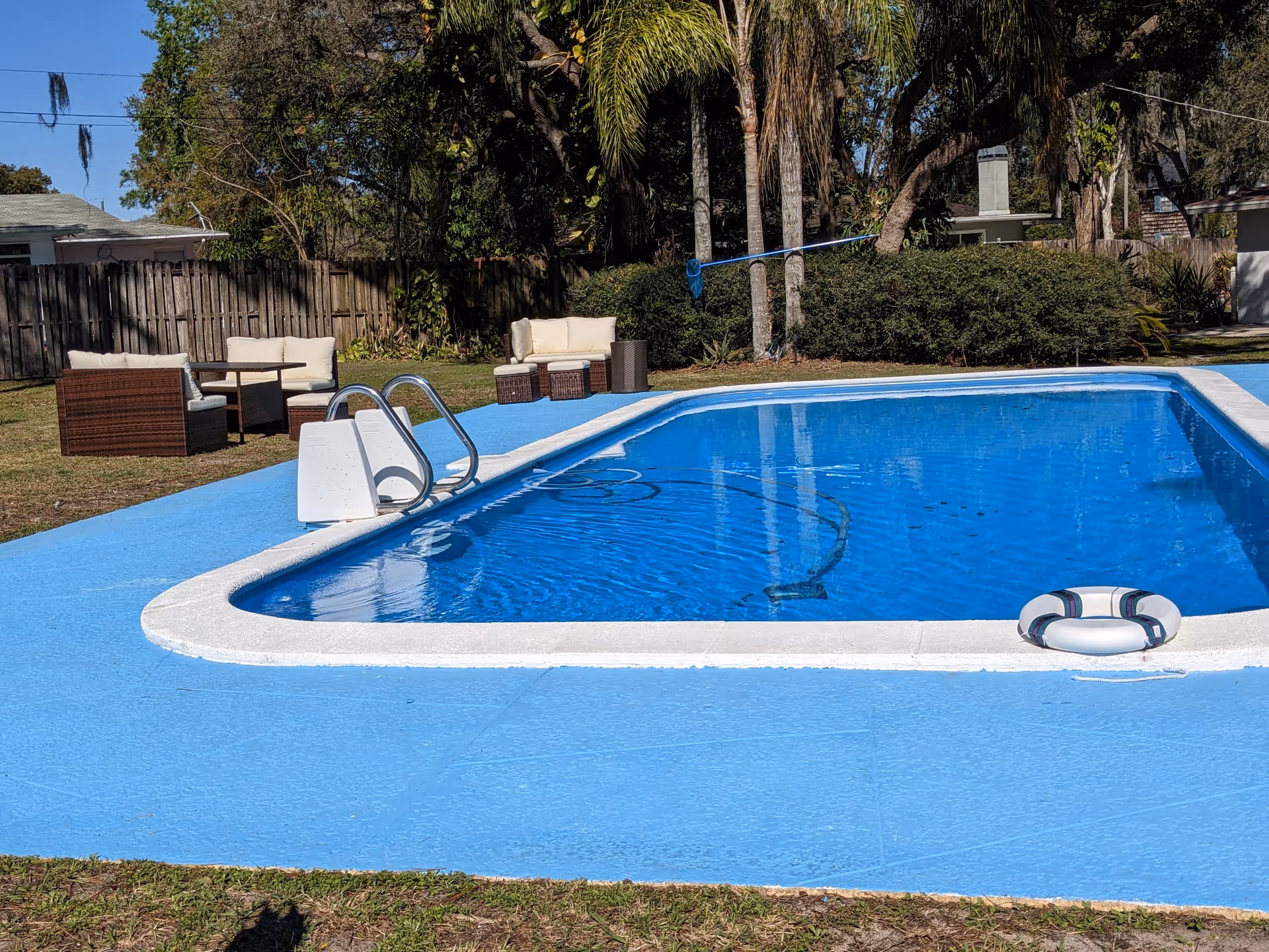 Outdoor pool area with blue water, seating, and greenery.